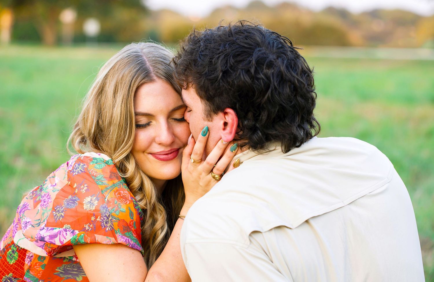 A romantic couple embraces in a sunny field with autumn colors in the background.
