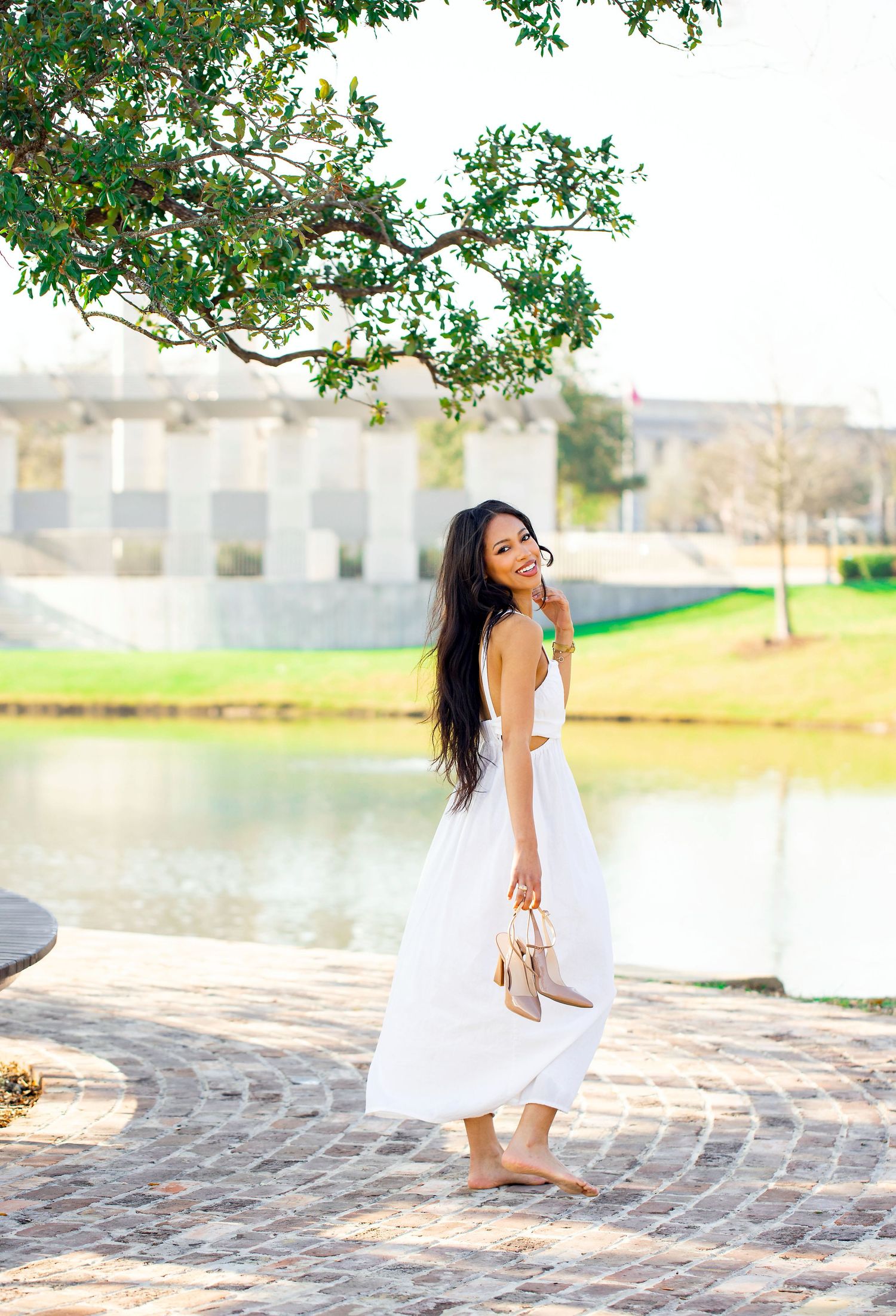 Joyful outdoor photo shoot by a lake with white flowing dress and natural scenery.