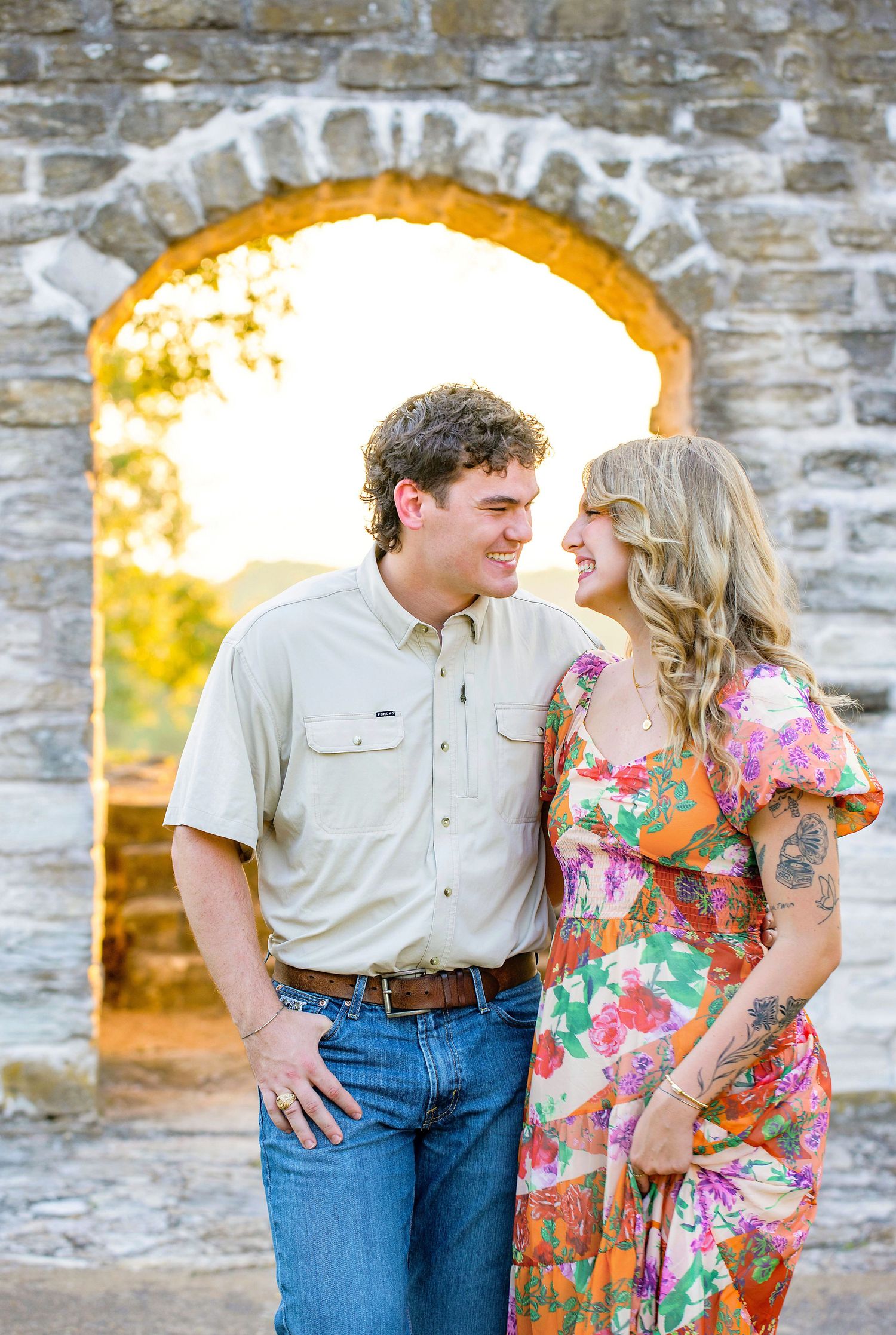 A couple shares romantic moments in front of a stone wall during a golden sunset photoshoot.