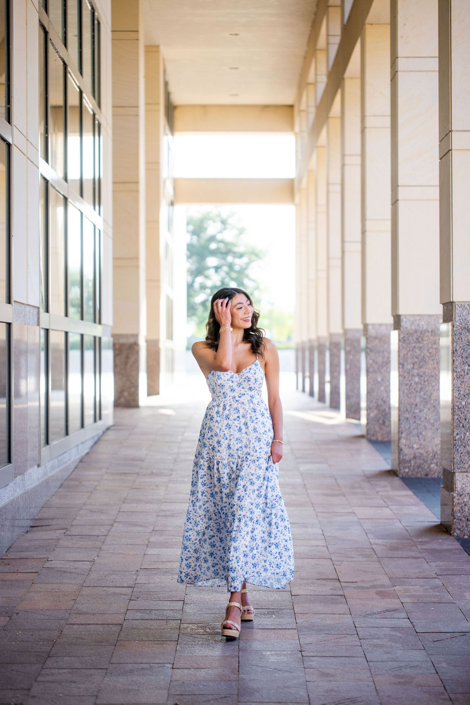 Texas A&M University graduate walking shots along a covered colonnade at George Bush Library in a floral summer dress.