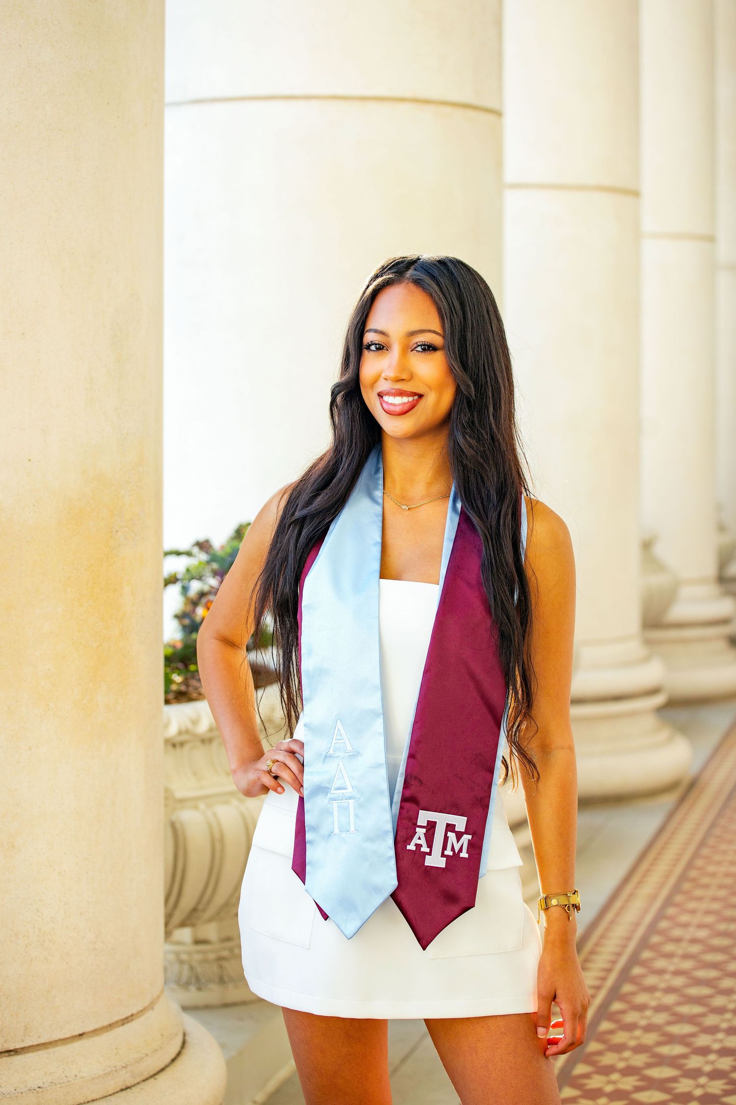 Graduate wearing white dress and burgundy stole poses confidently in front of classical columns.