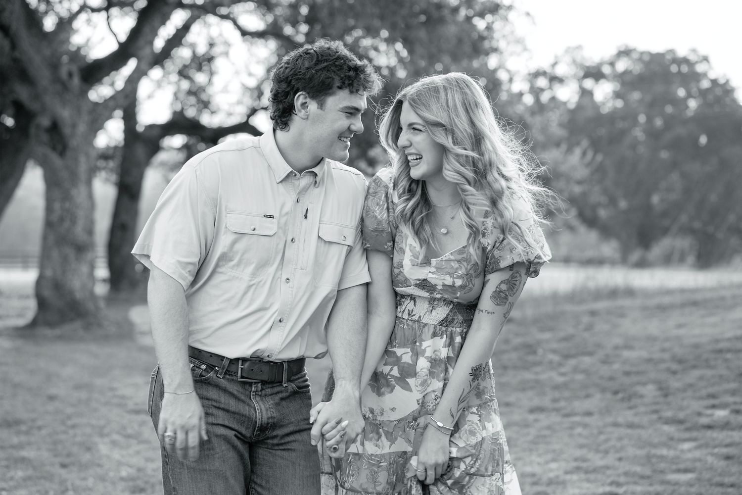 A couple in casual attire shares a romantic moment together during an outdoor photoshoot in a grassy field.