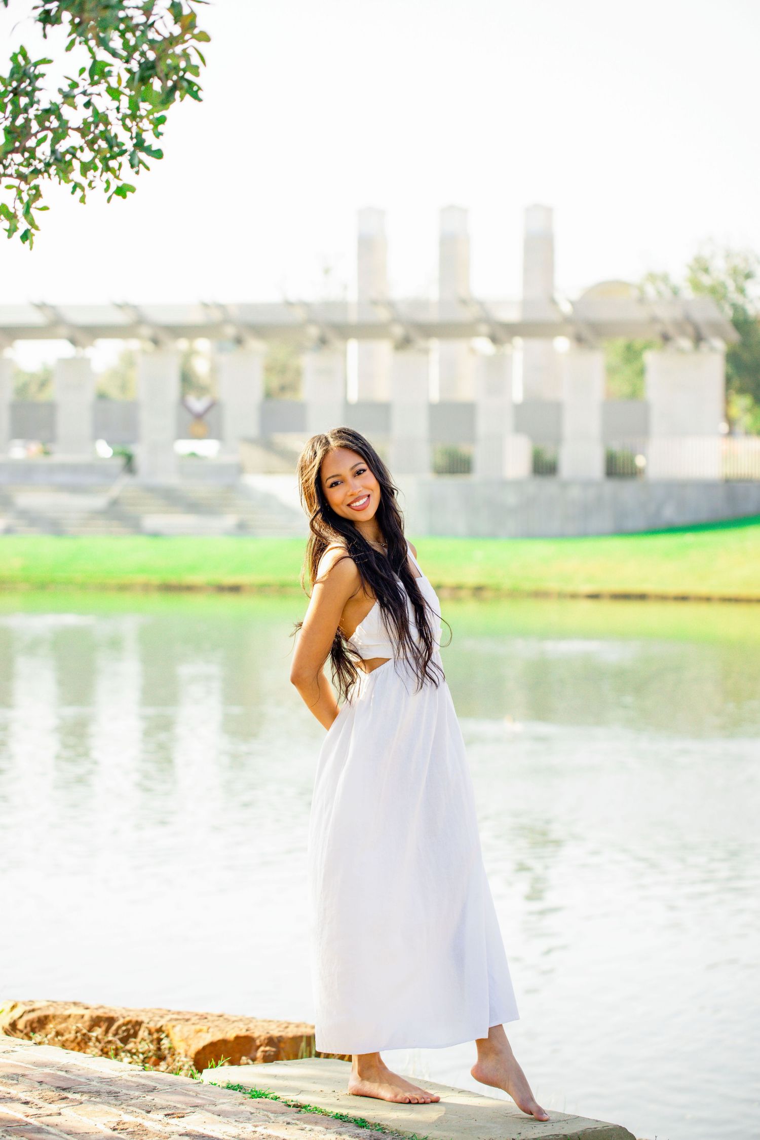 A flowing white sundress styled for a summer photoshoot near a lake with architectural elements in background.