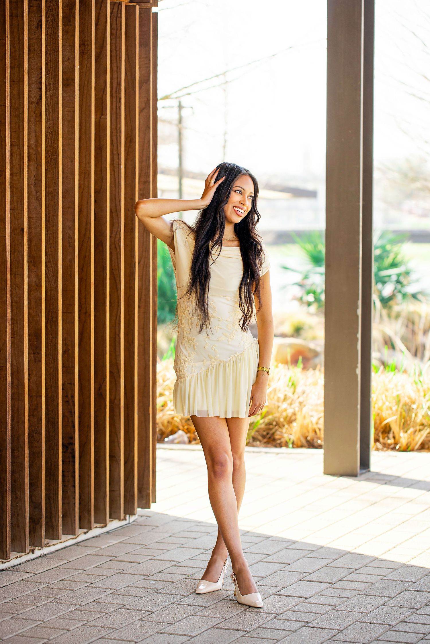 A short white pleated dress styled with heels for a fashion photo against wooden slat wall backdrop.