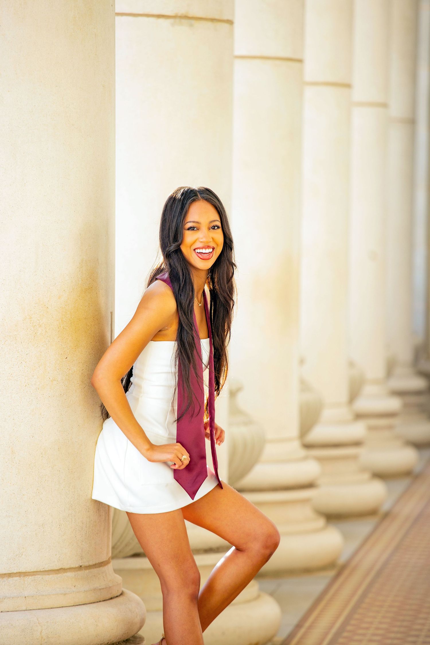 Candid graduation portraits captured between elegant white columns with natural lighting.