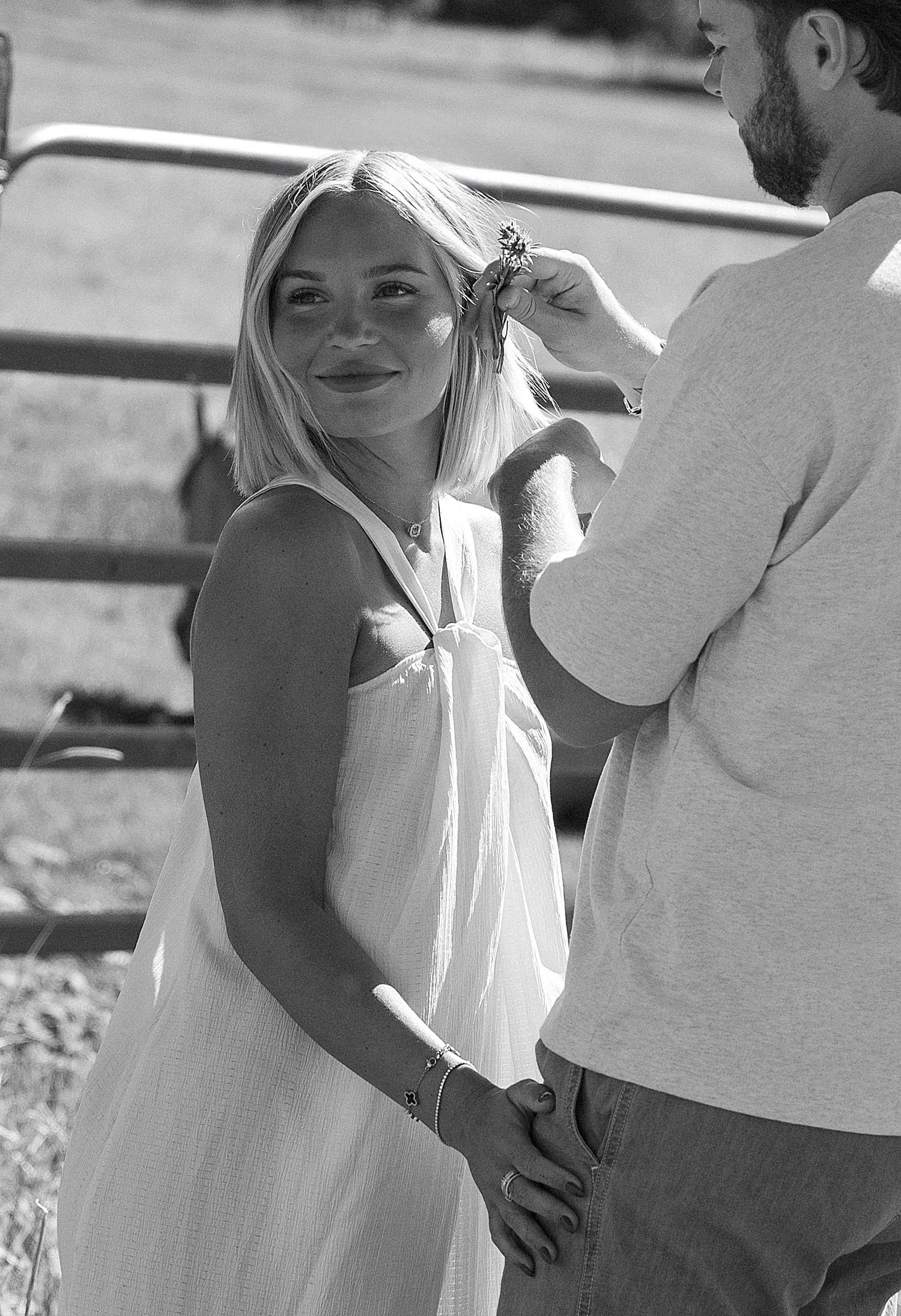 Black and white photo of a smiling blonde woman in a white dress holding hands with a man outdoors.