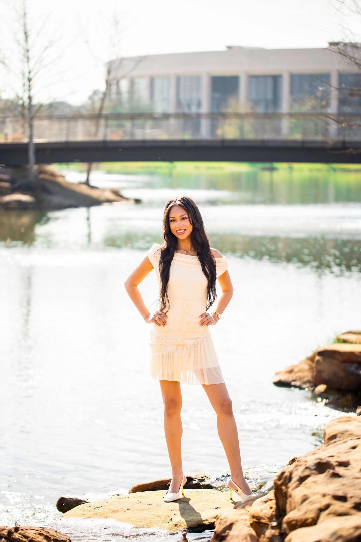 A photoshoot series by a lakeside with rocky shoreline showing poses in a white summer dress.