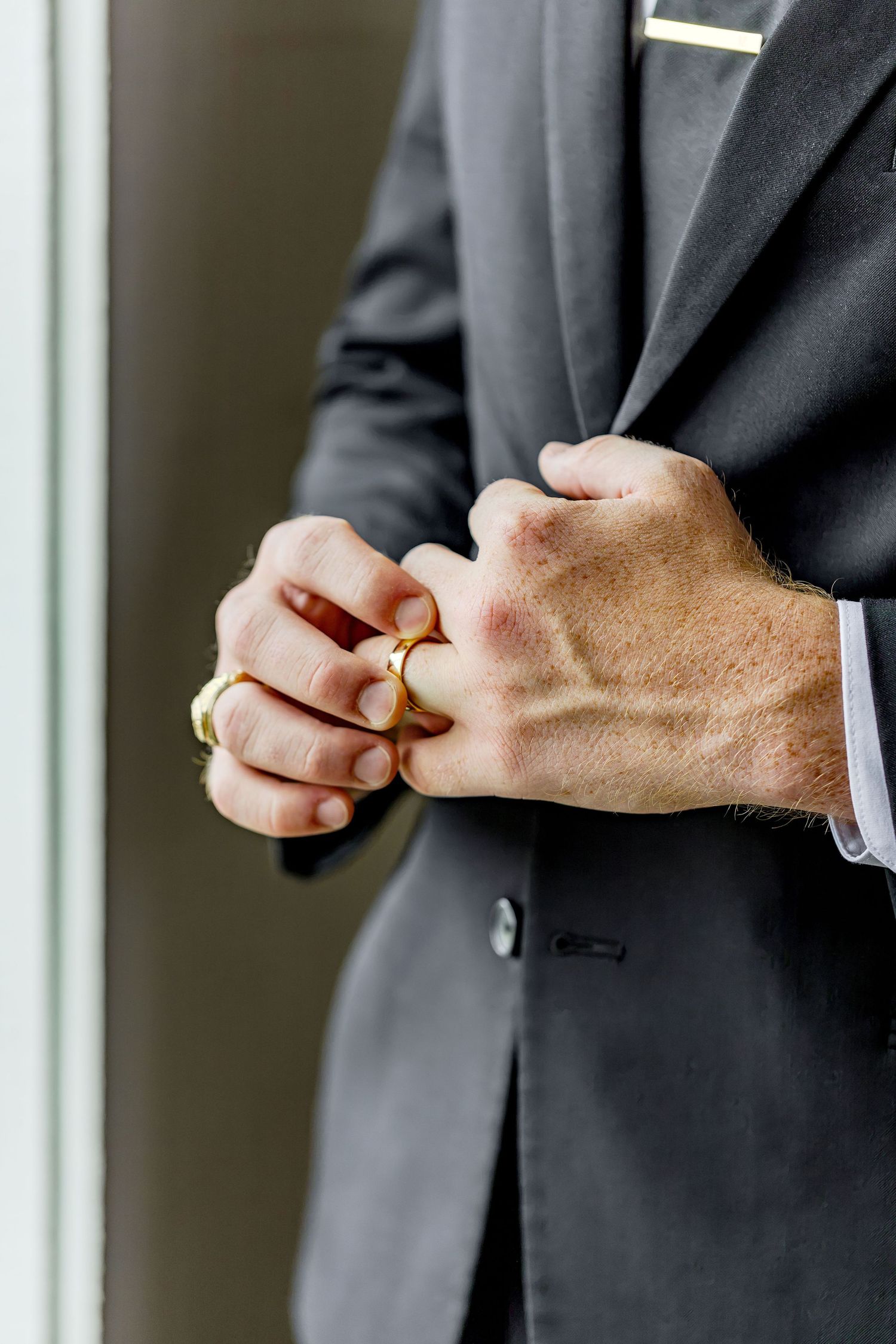 Man in dark suit holding two gold wedding rings, close-up of hands showing ring details.