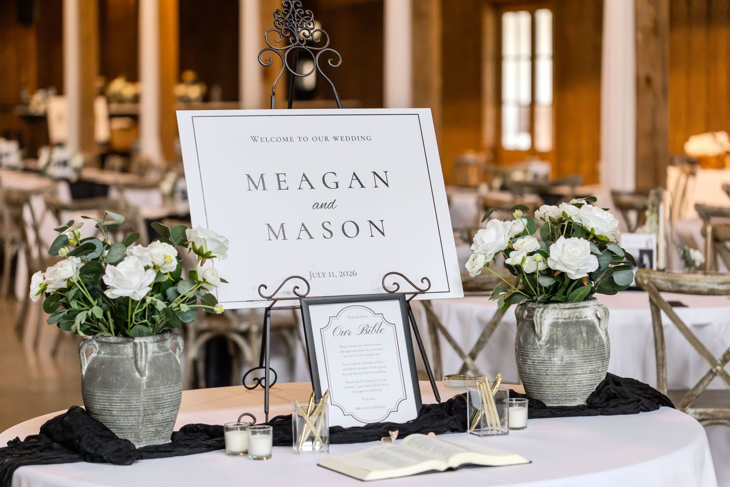 Elegant wedding welcome sign for Meagan and Mason with white floral arrangements and black accents on a draped table.