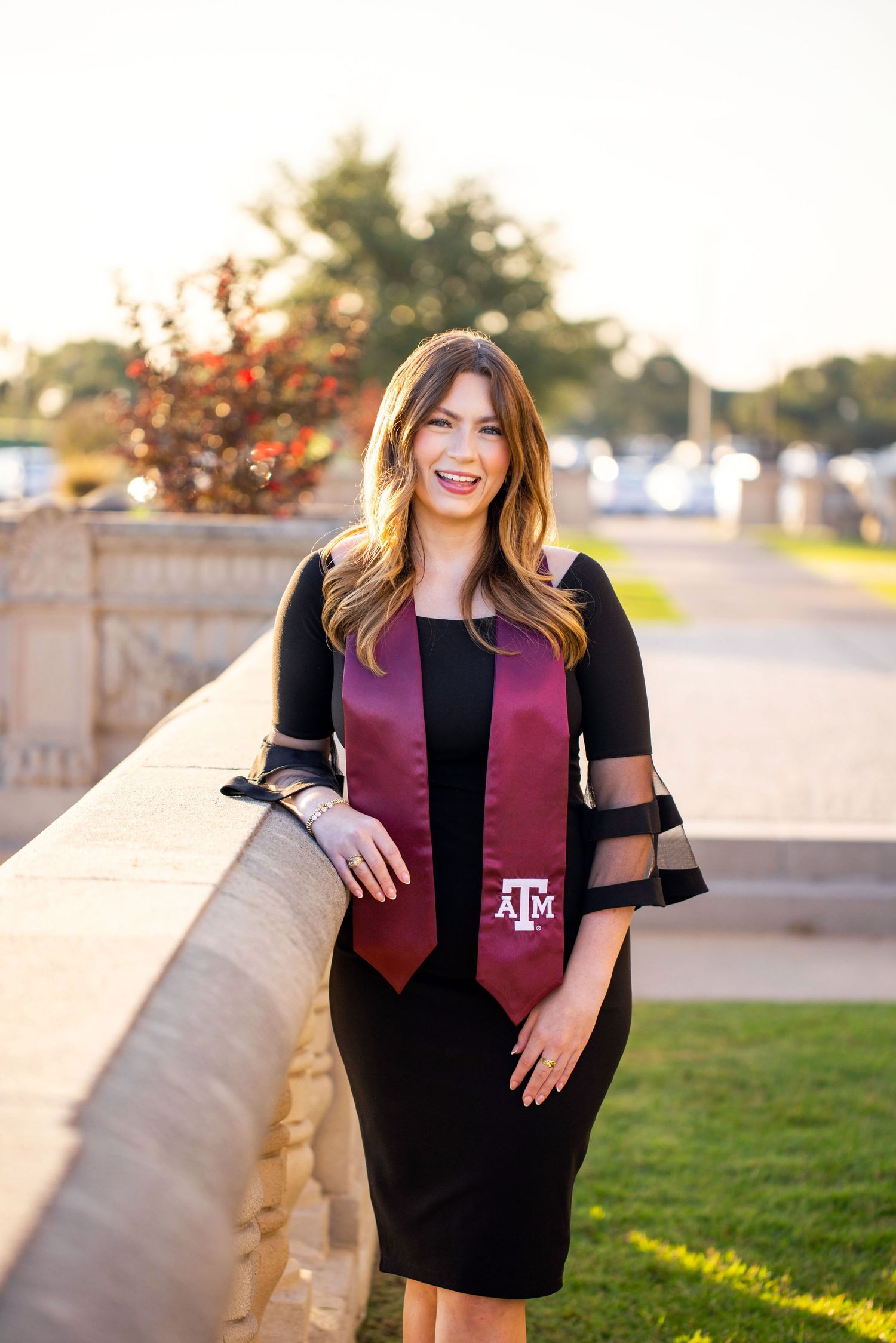 A young woman with long brown hair wearing a black and purple outfit smiles while standing outdoors.
