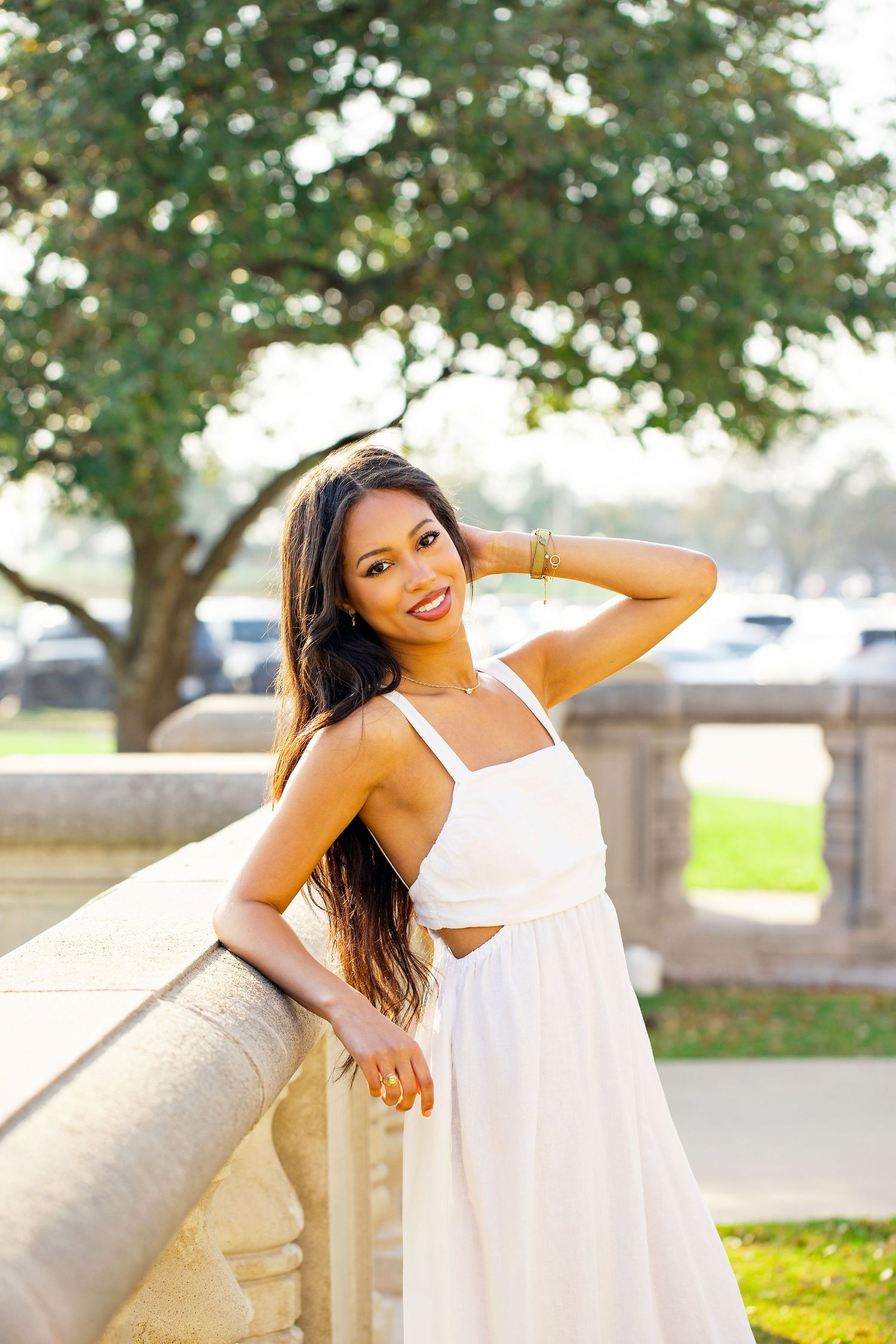 Outdoor portrait session featuring white summer dress against architectural backdrop and trees.