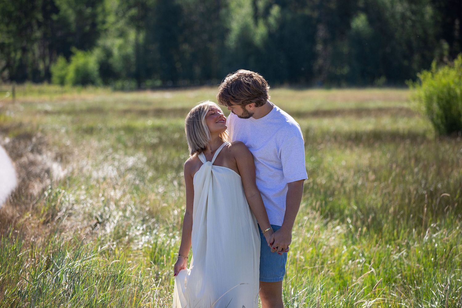 A romantic couple sharing a tender kiss in a sunlit meadow, with lush green trees in the background.