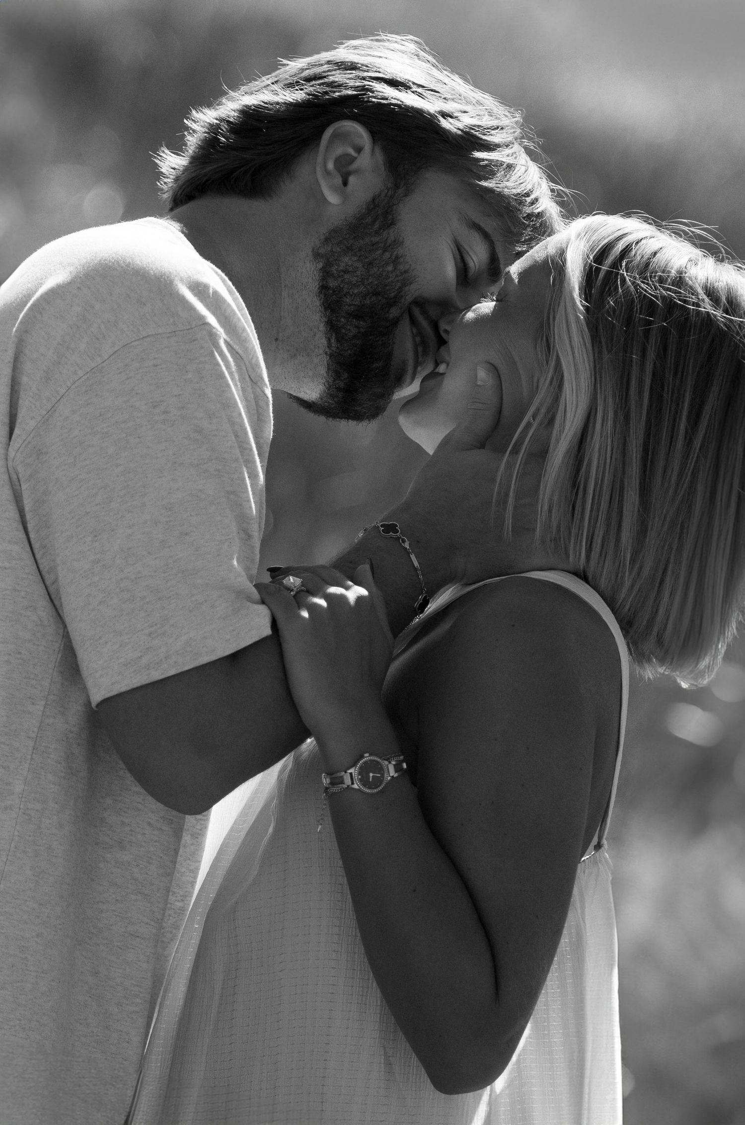 Black and white photo of a couple sharing a romantic kiss outdoors, woman wearing a watch and bracelet.