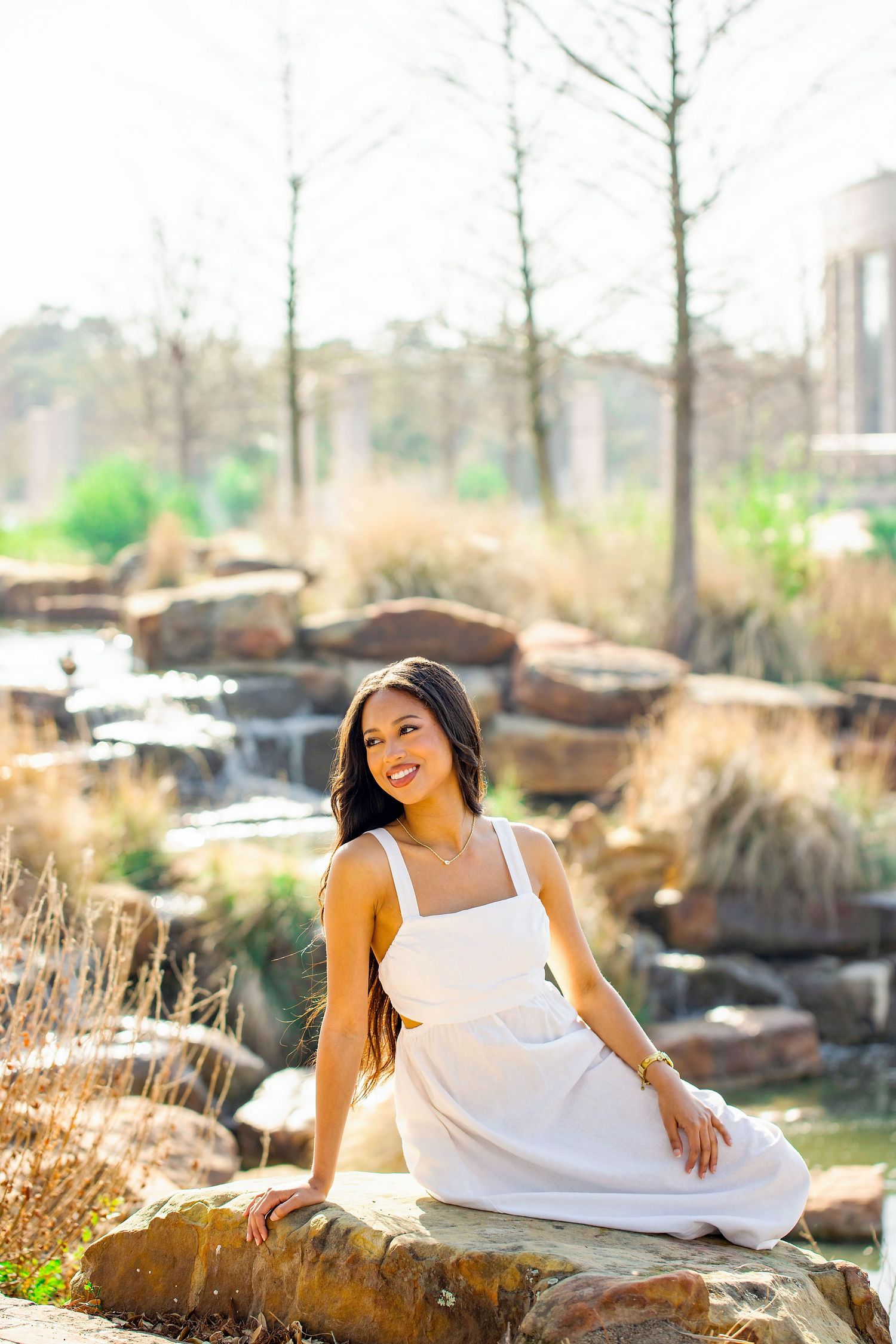A person in a white dress poses gracefully on natural rock formations during an outdoor photo session.