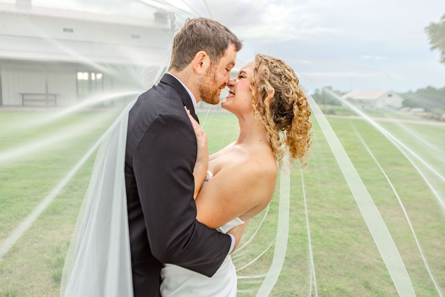 Bride and groom sharing a romantic moment under a flowing veil outdoors on their wedding day.