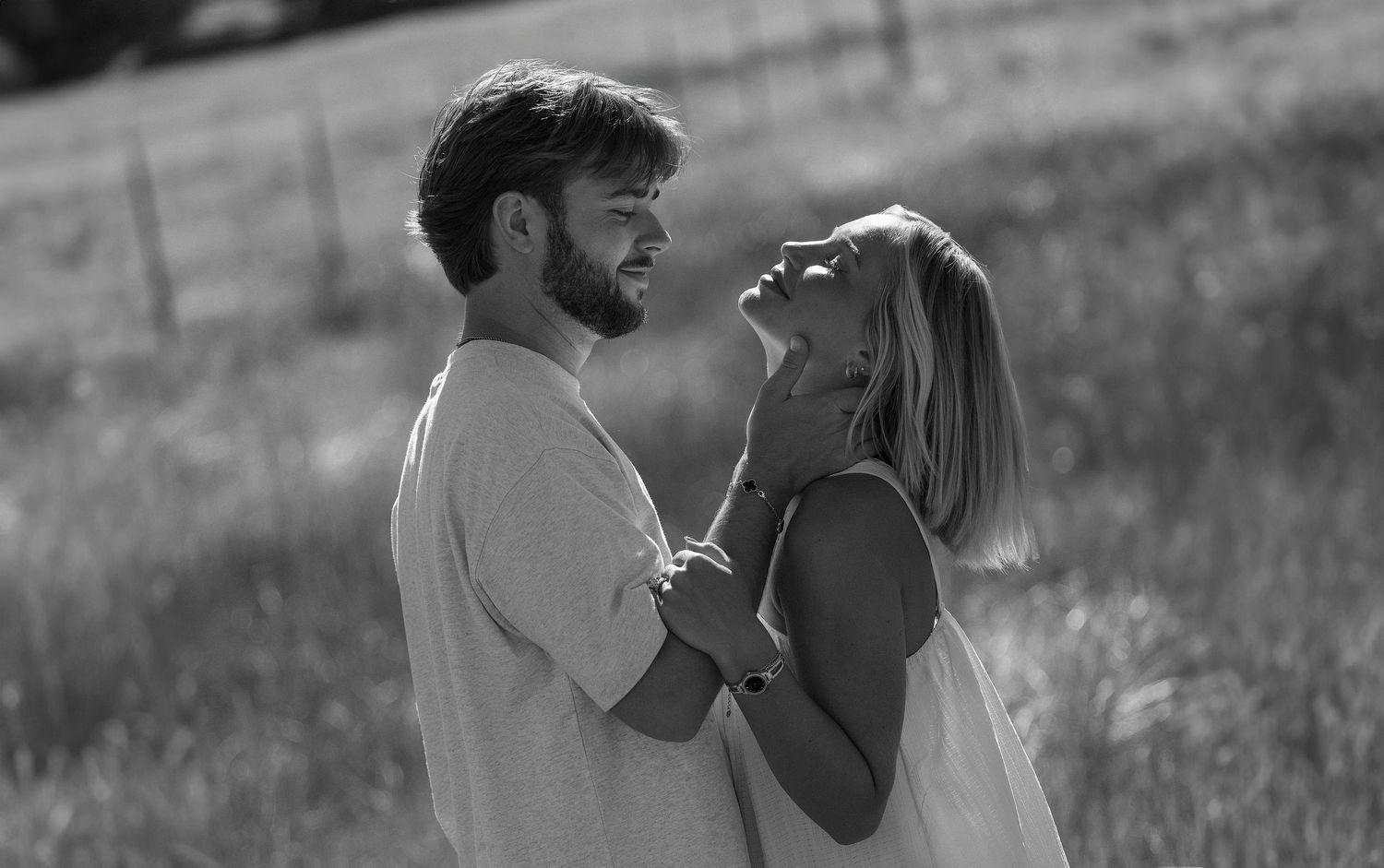 Black and white photo of a romantic couple embracing in a field, woman laughing joyfully as man holds her face tenderly.