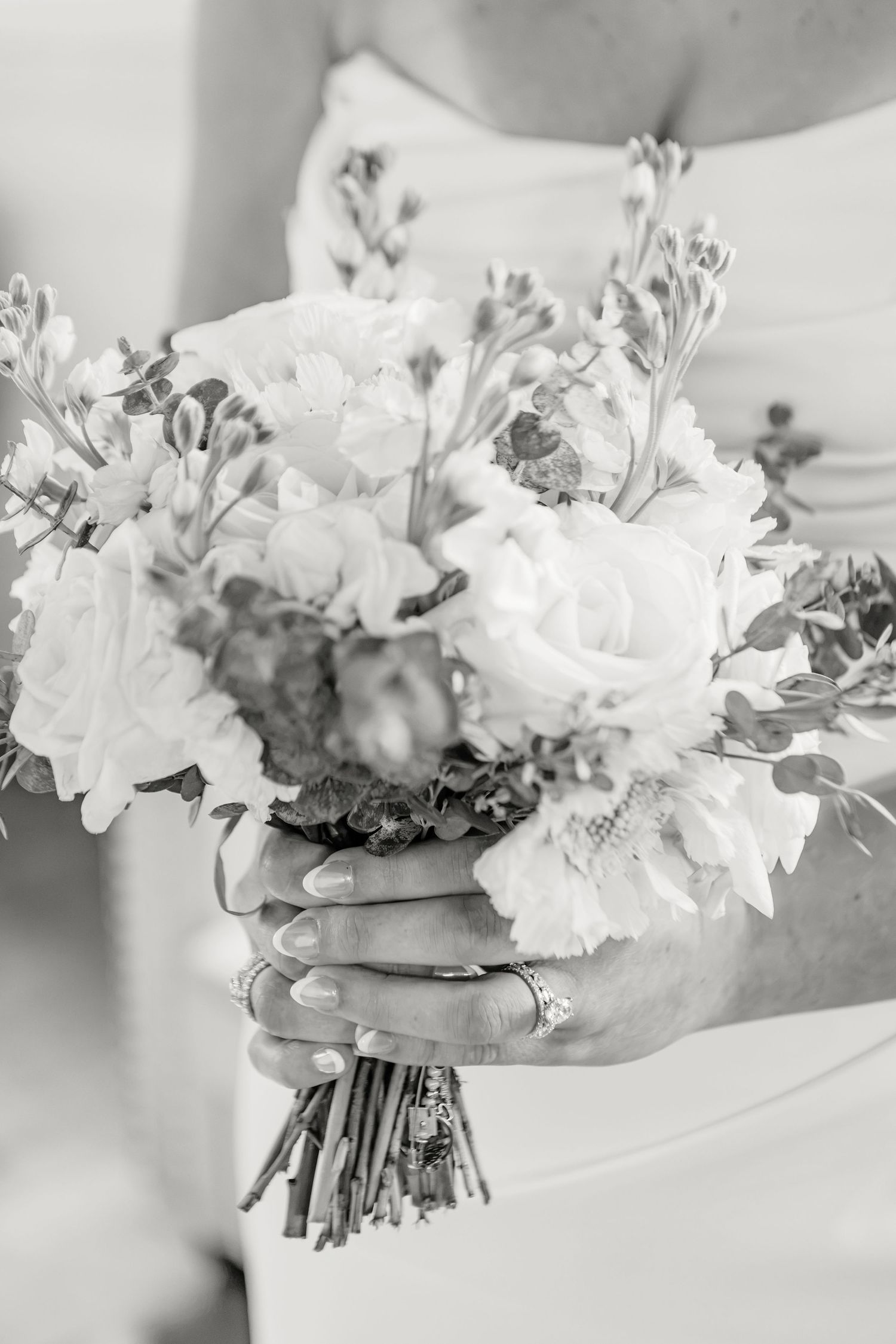 Black and white photo of a bride holding a beautiful bouquet of roses and wildflowers, with an engagement ring visible.