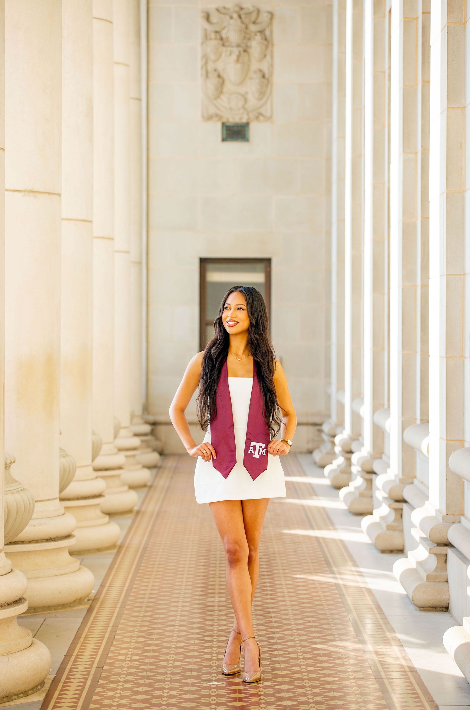 A white summer dress contrasts beautifully against classical stone columns in an elegant architectural setting.