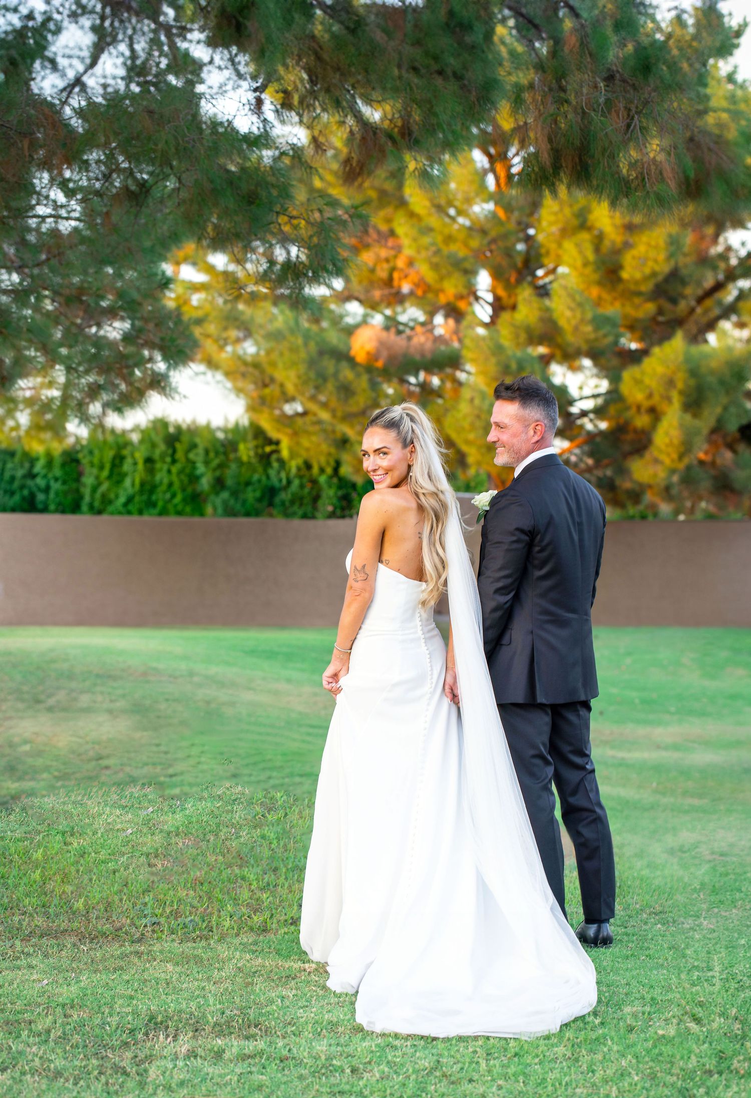 Wedding couple poses in garden setting with autumn trees creating a colorful backdrop in Scottsdale, Arizona.