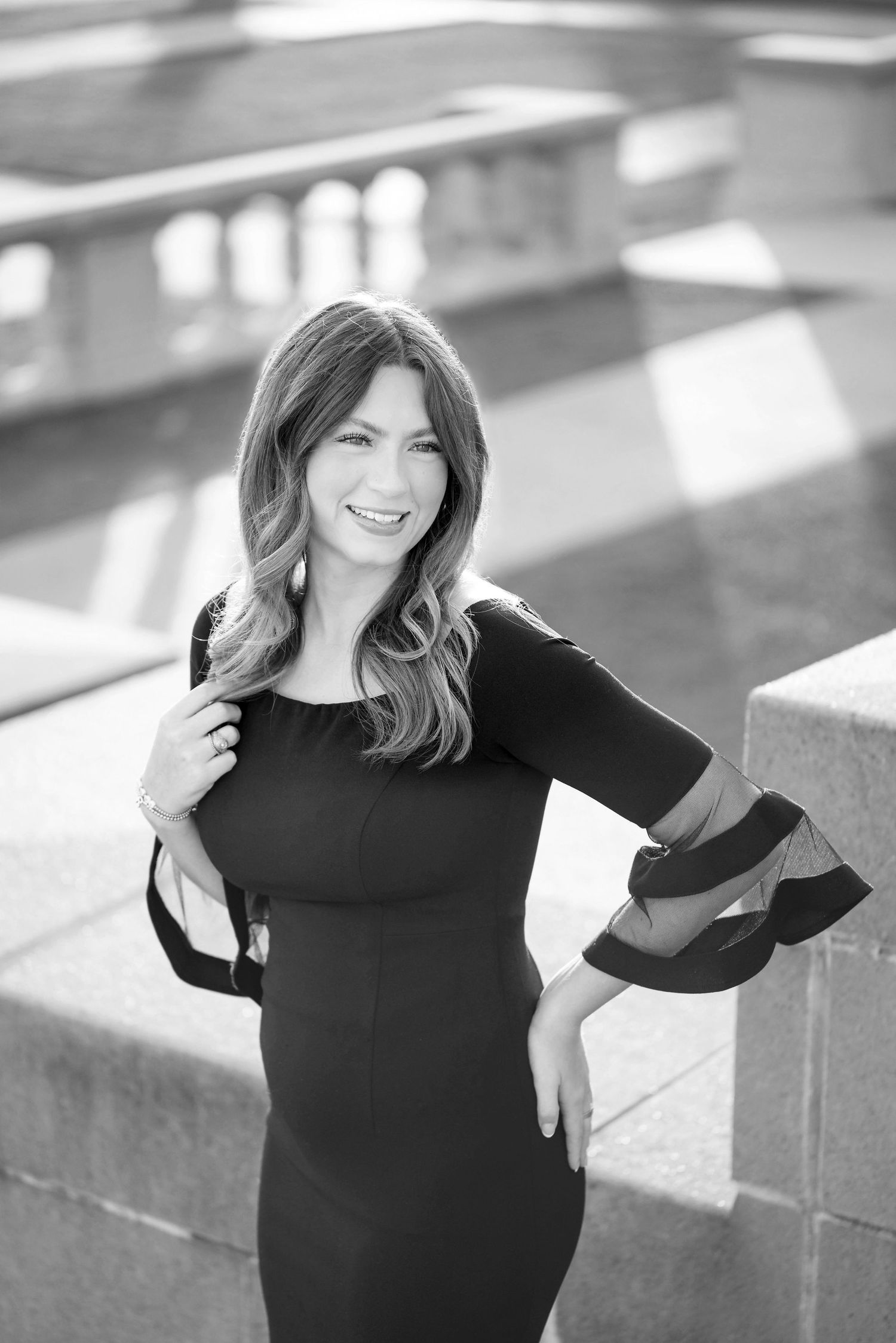 A smiling woman with long wavy hair wearing a black dress poses in front of a building.