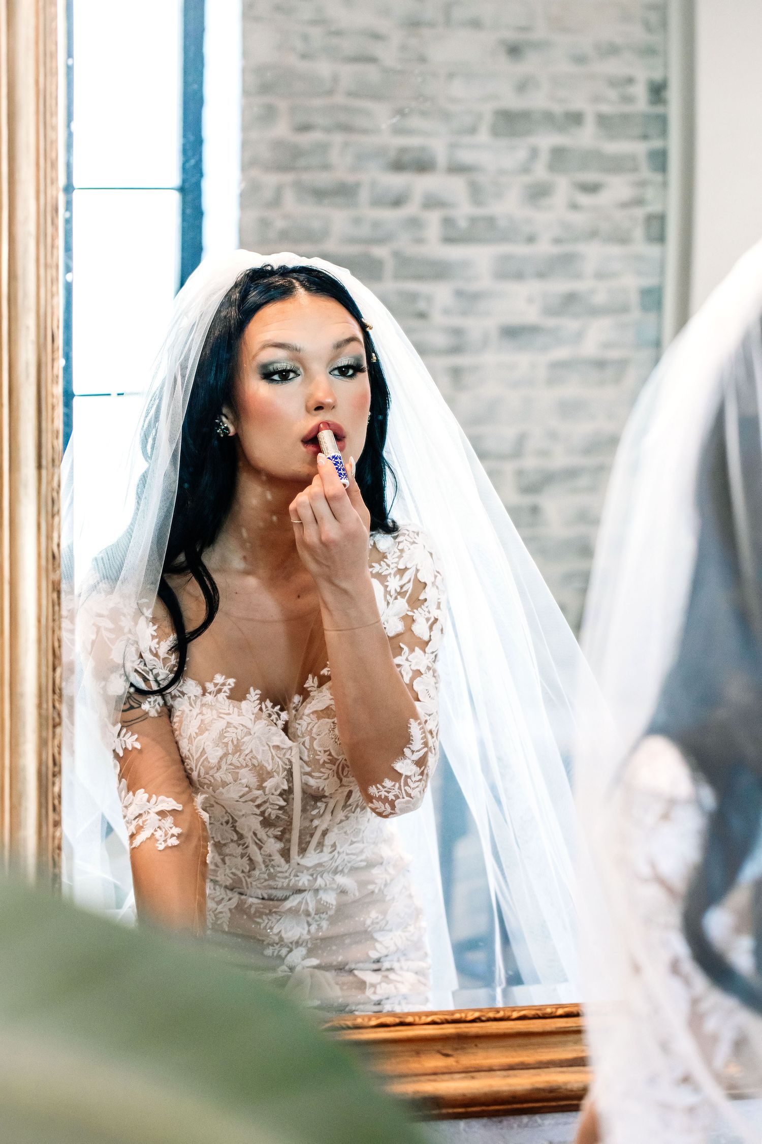 A bride in a delicate lace wedding gown with long sleeves is captured in an emotional moment before a mirror.