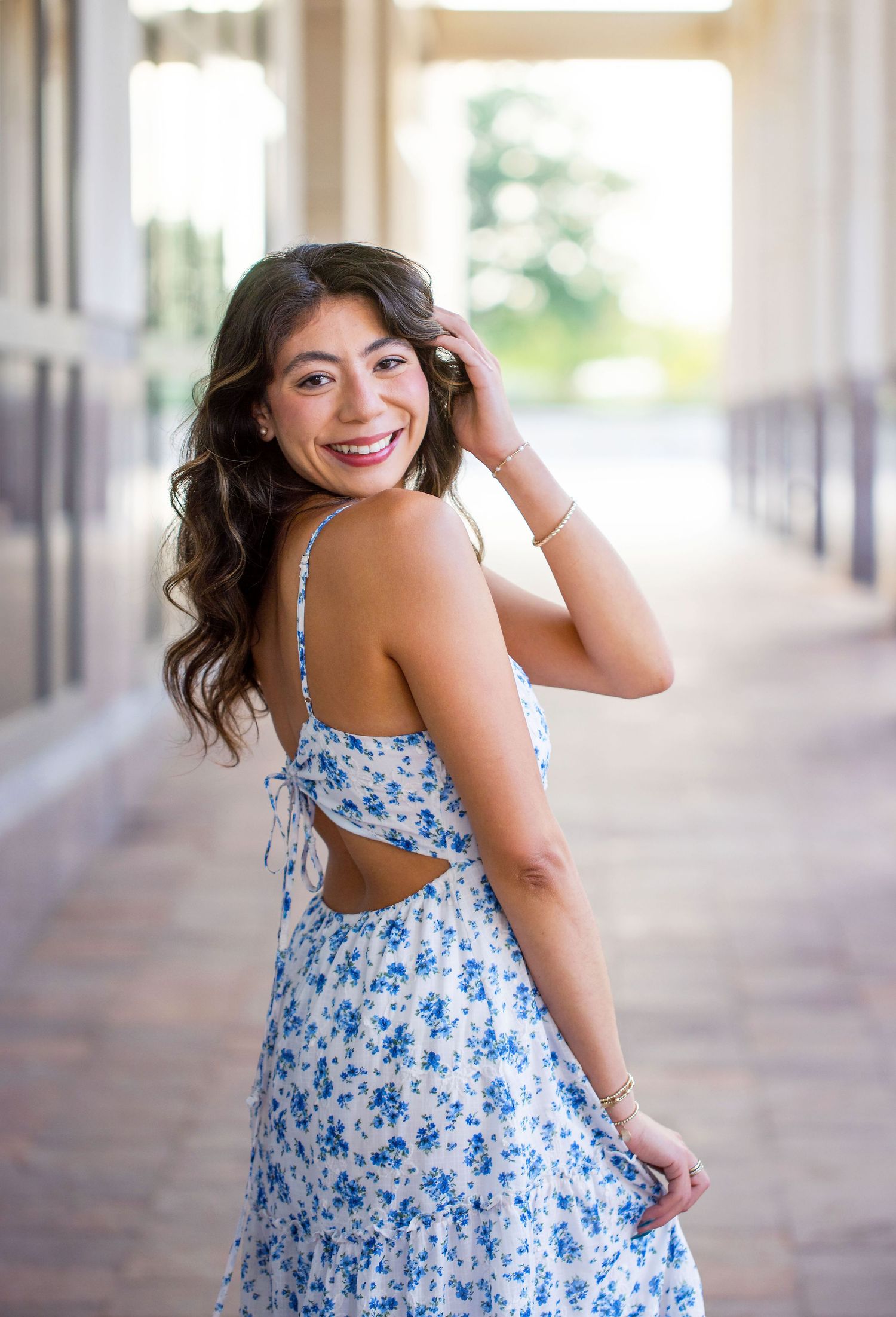 Texas A&M University graduate in a blue floral summer dress captured in a sunlit outdoor corridor.