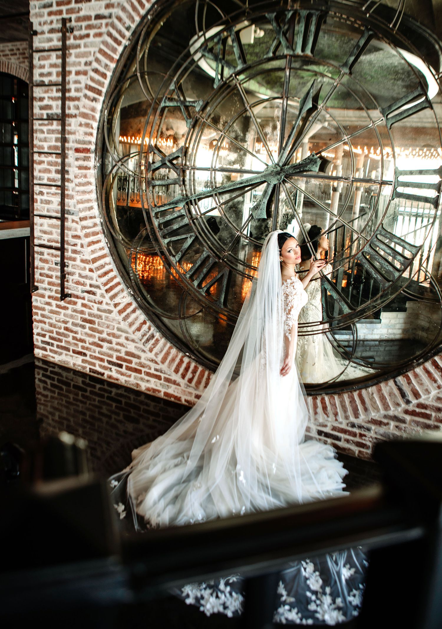 A white wedding dress hangs elegantly against a rustic brick wall with large circular mirrors creating a dramatic backdrop.