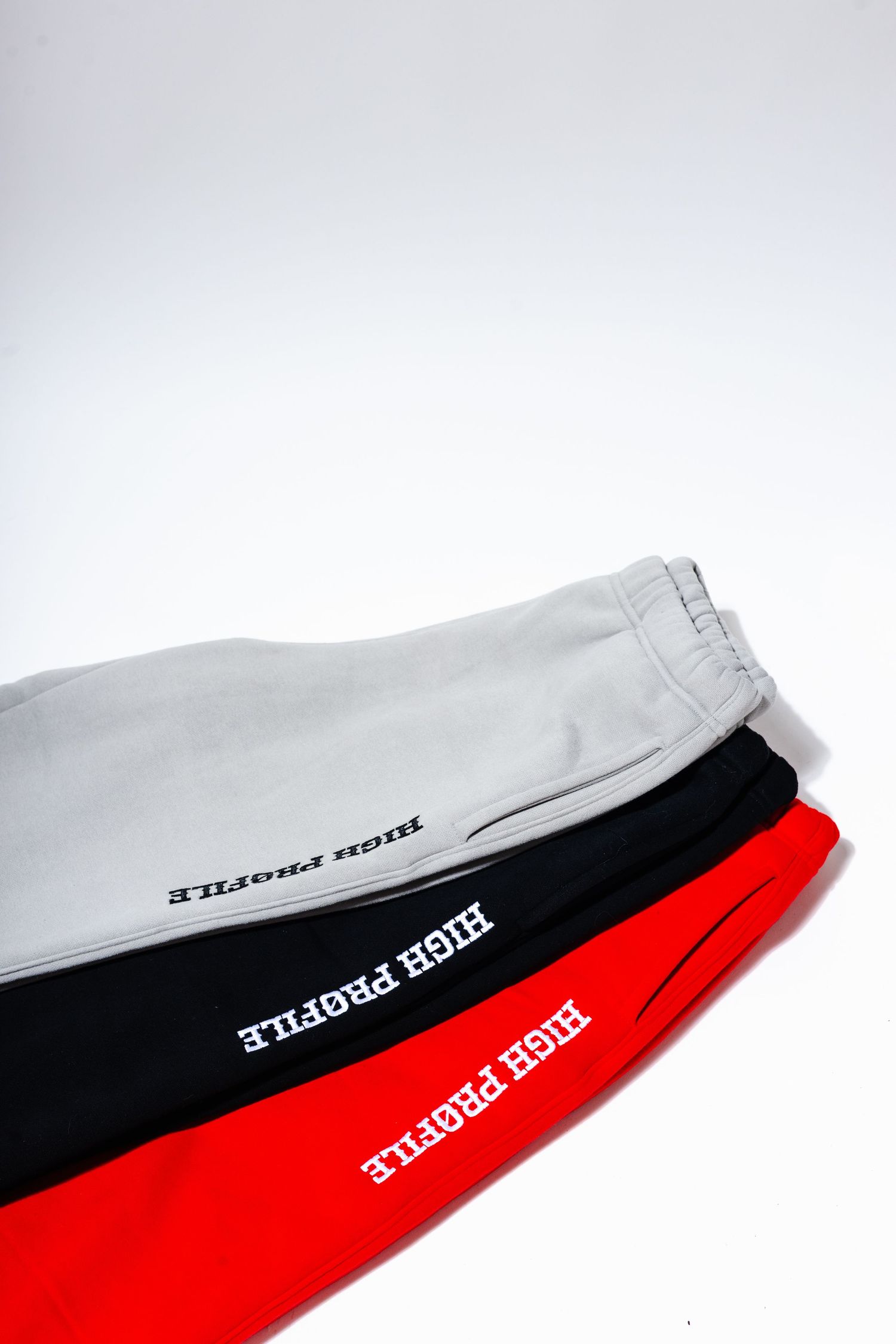 Three pairs of sweatpants in grey, black and red featuring High Profile text branding displayed on clean background.