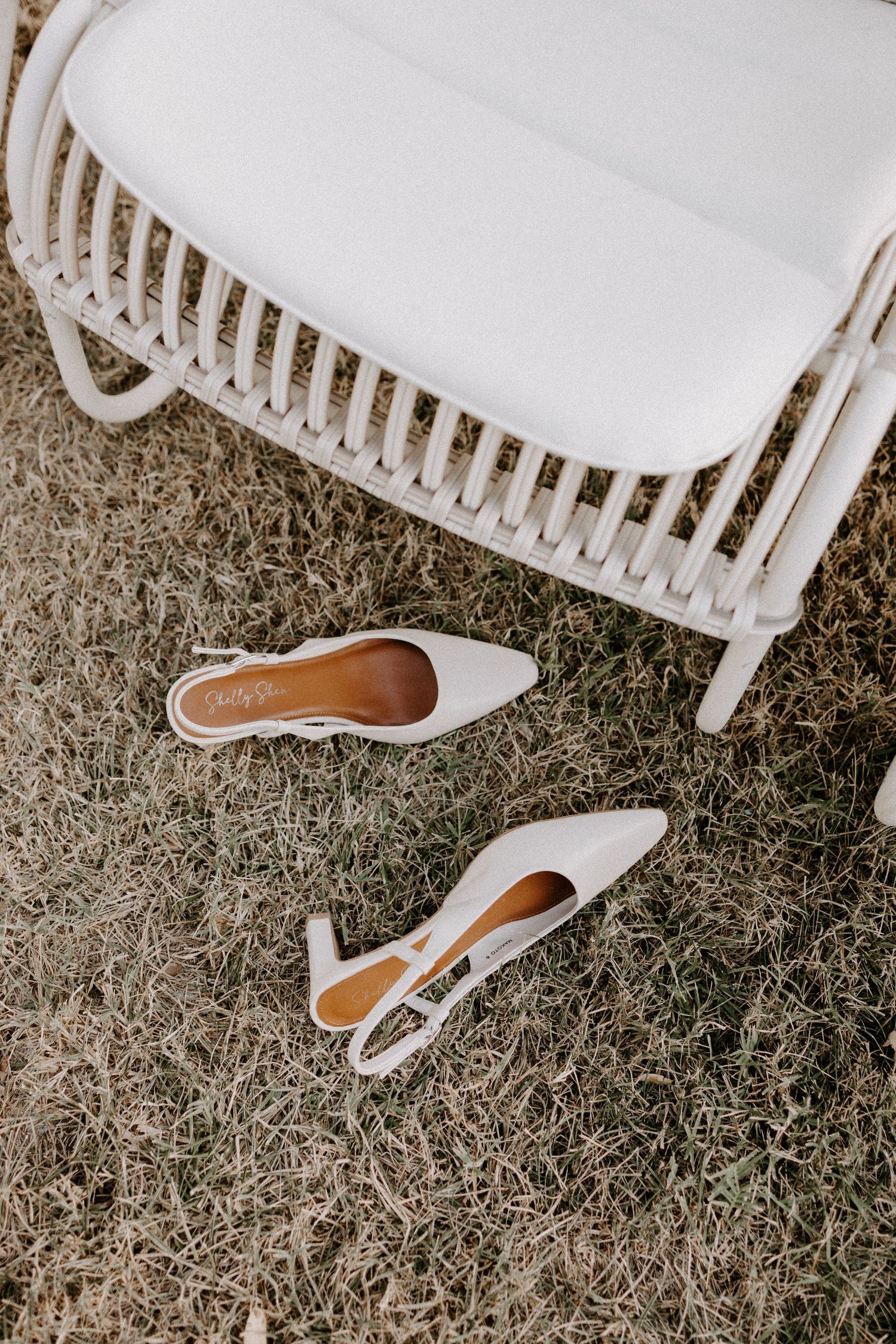 White bridal shoes displayed on grass against a white chair.