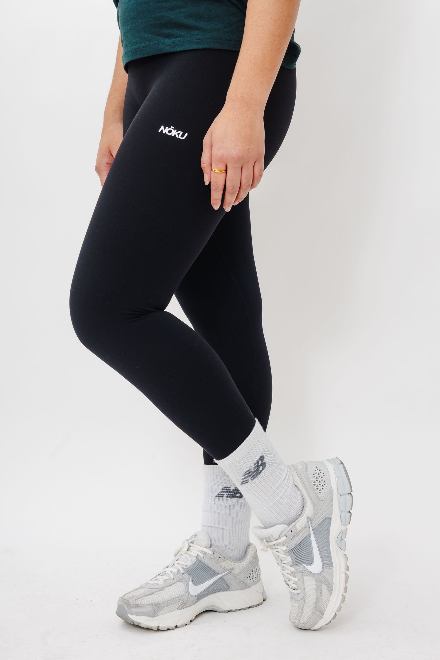 Close-up view of legs wearing black leggings and white Nike athletic sneakers against a white background.