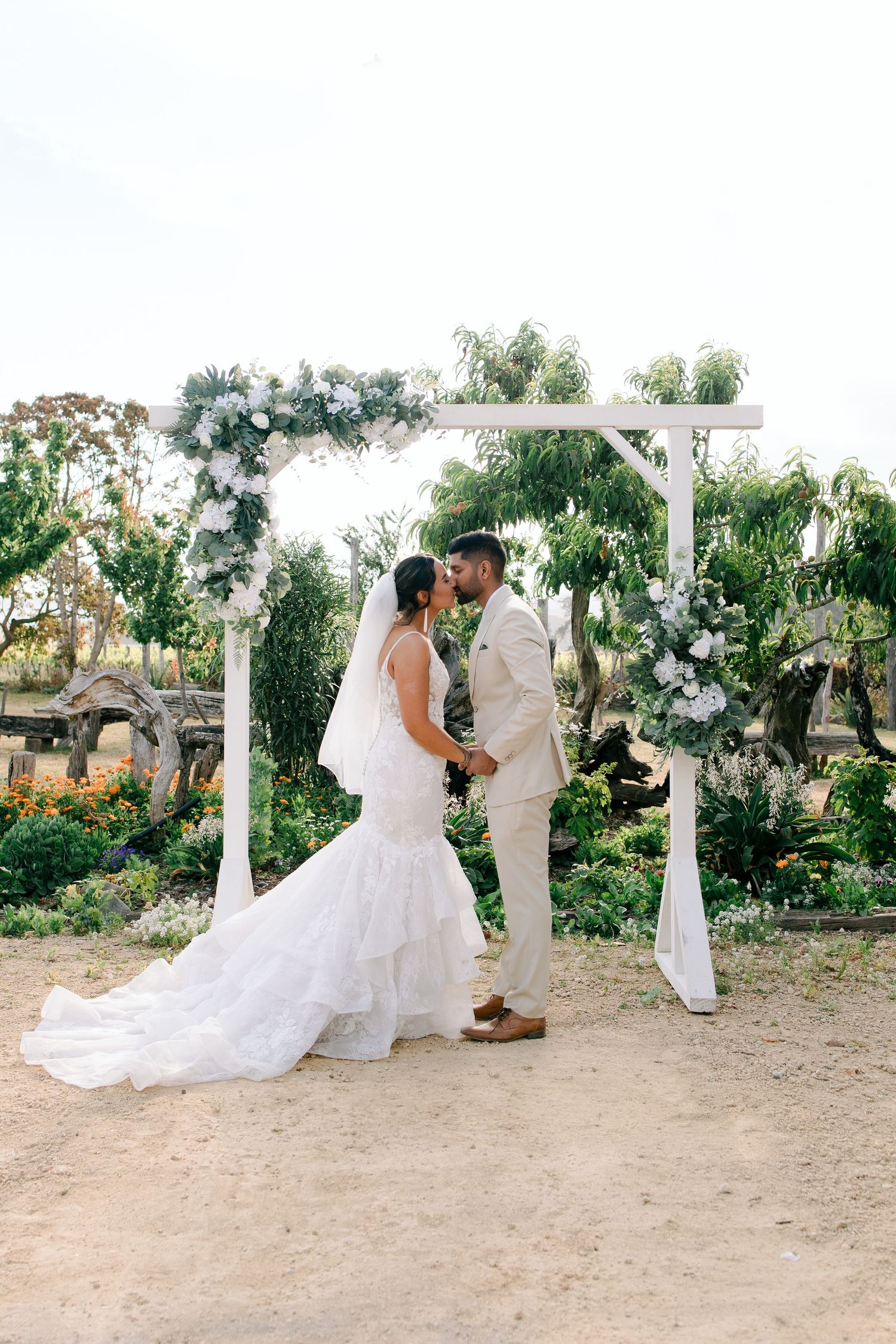 A wedding couple shares an intimate moment during their outdoor beach ceremony under white draped arches.