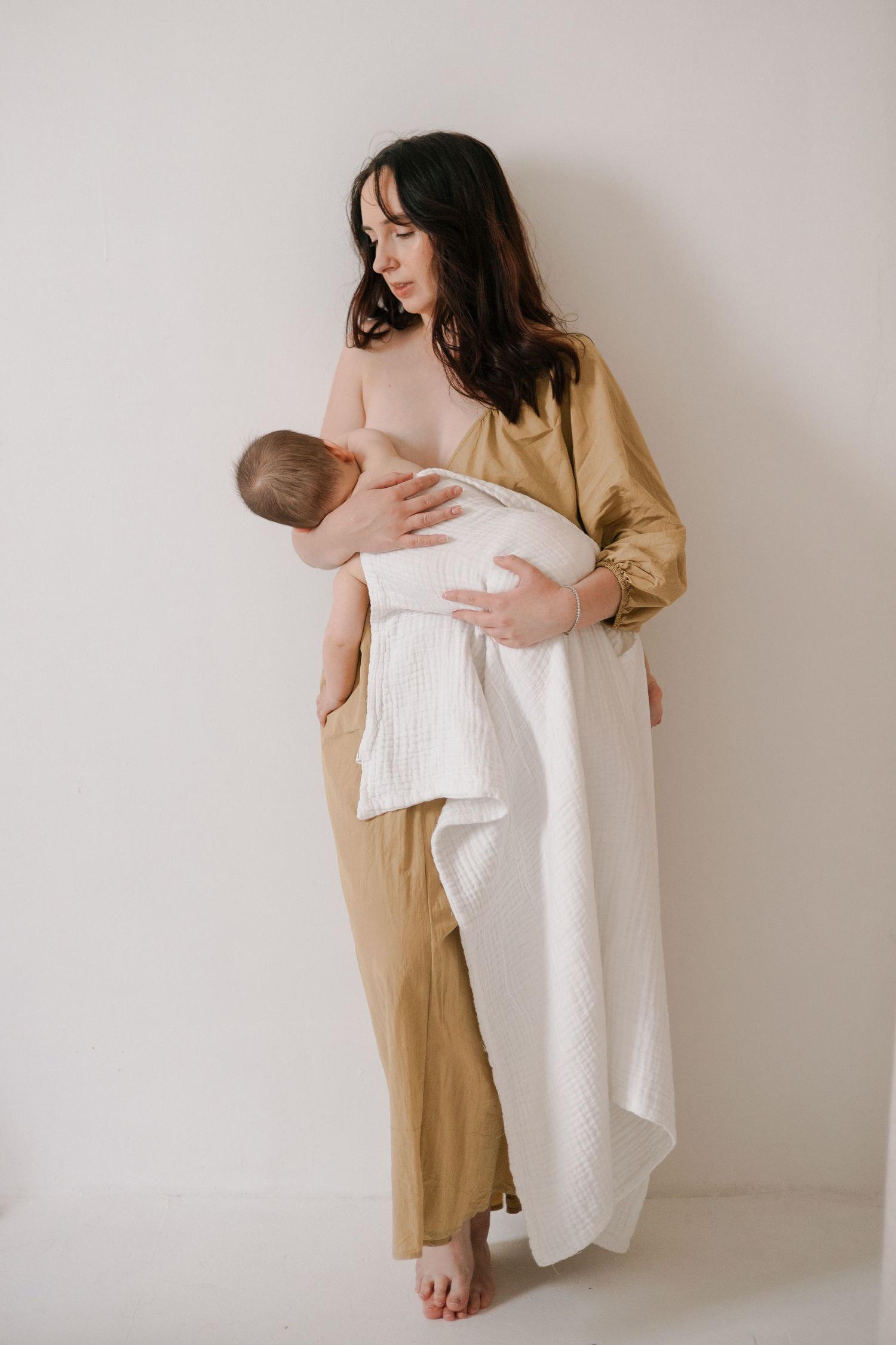 A series of four minimalist photos showing a person in beige clothing holding white fabric against a neutral wall.