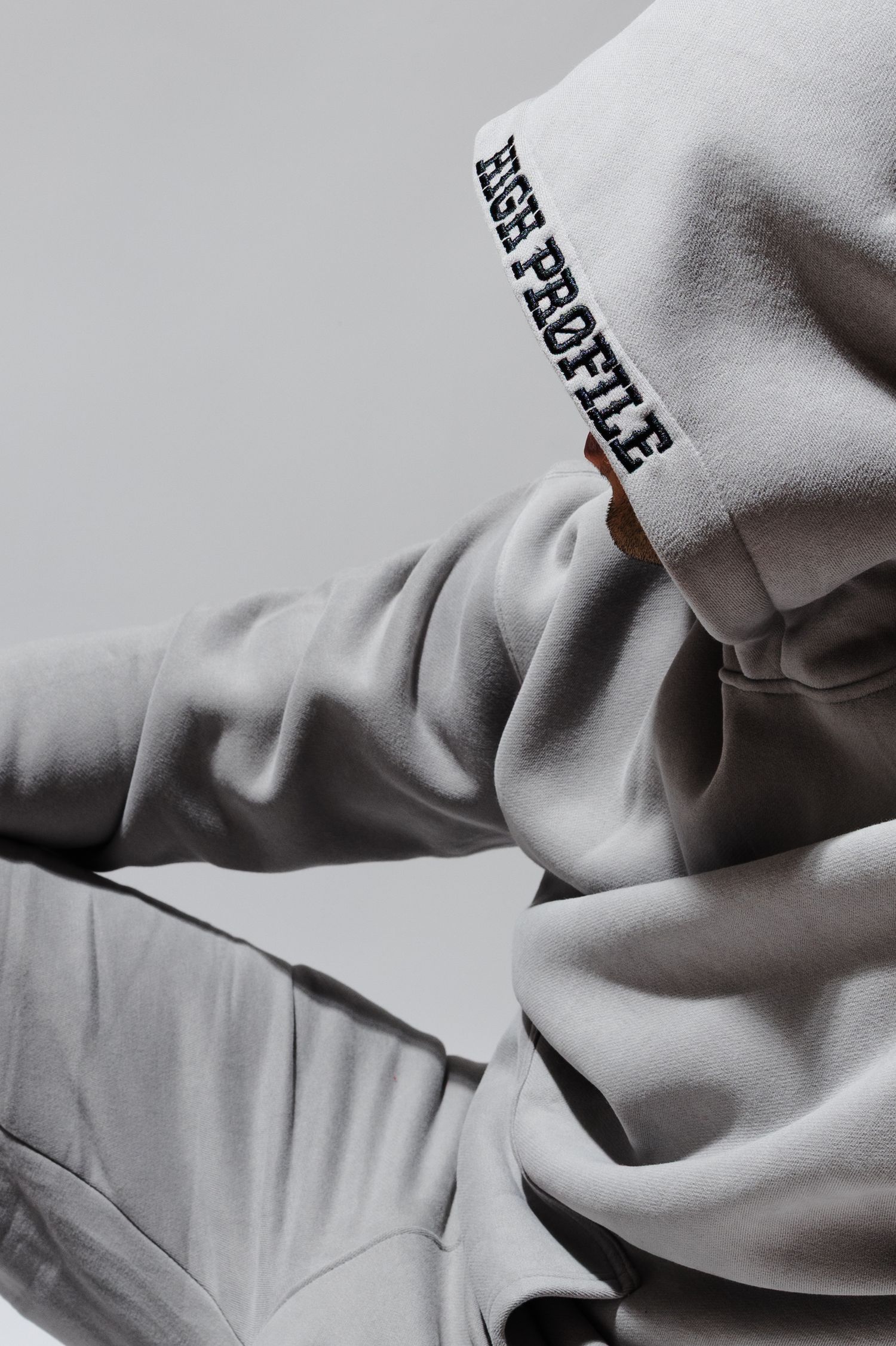 Close-up shot of a light gray hoodie sweatshirt showing folded fabric and partial text detail on the sleeve.