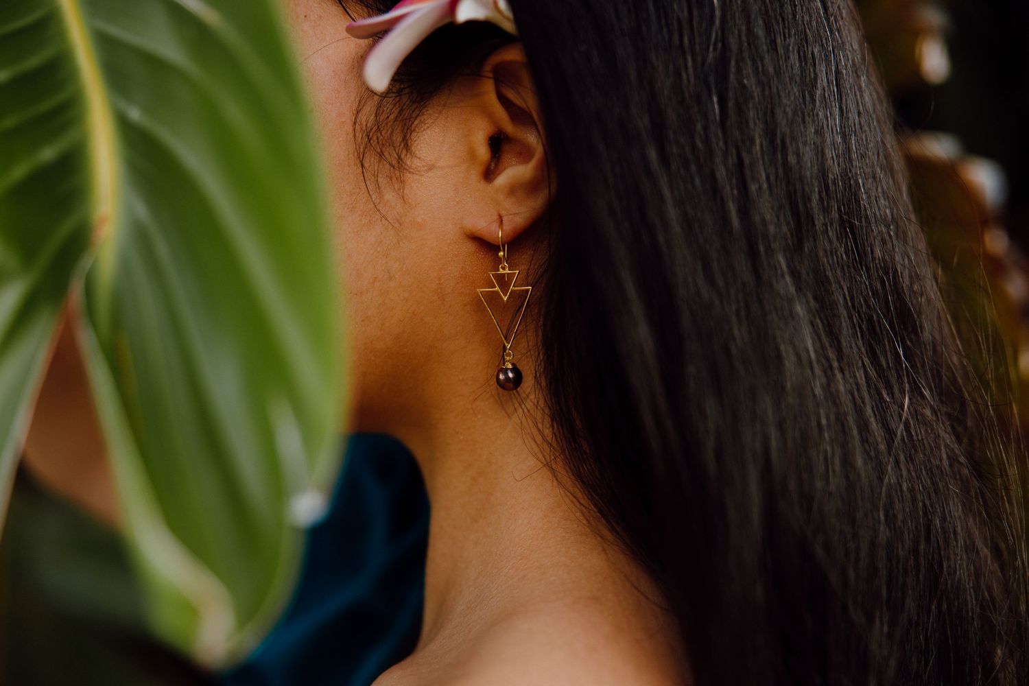 Three delicate gold hoops and dangle earrings displayed against a blurred natural background.