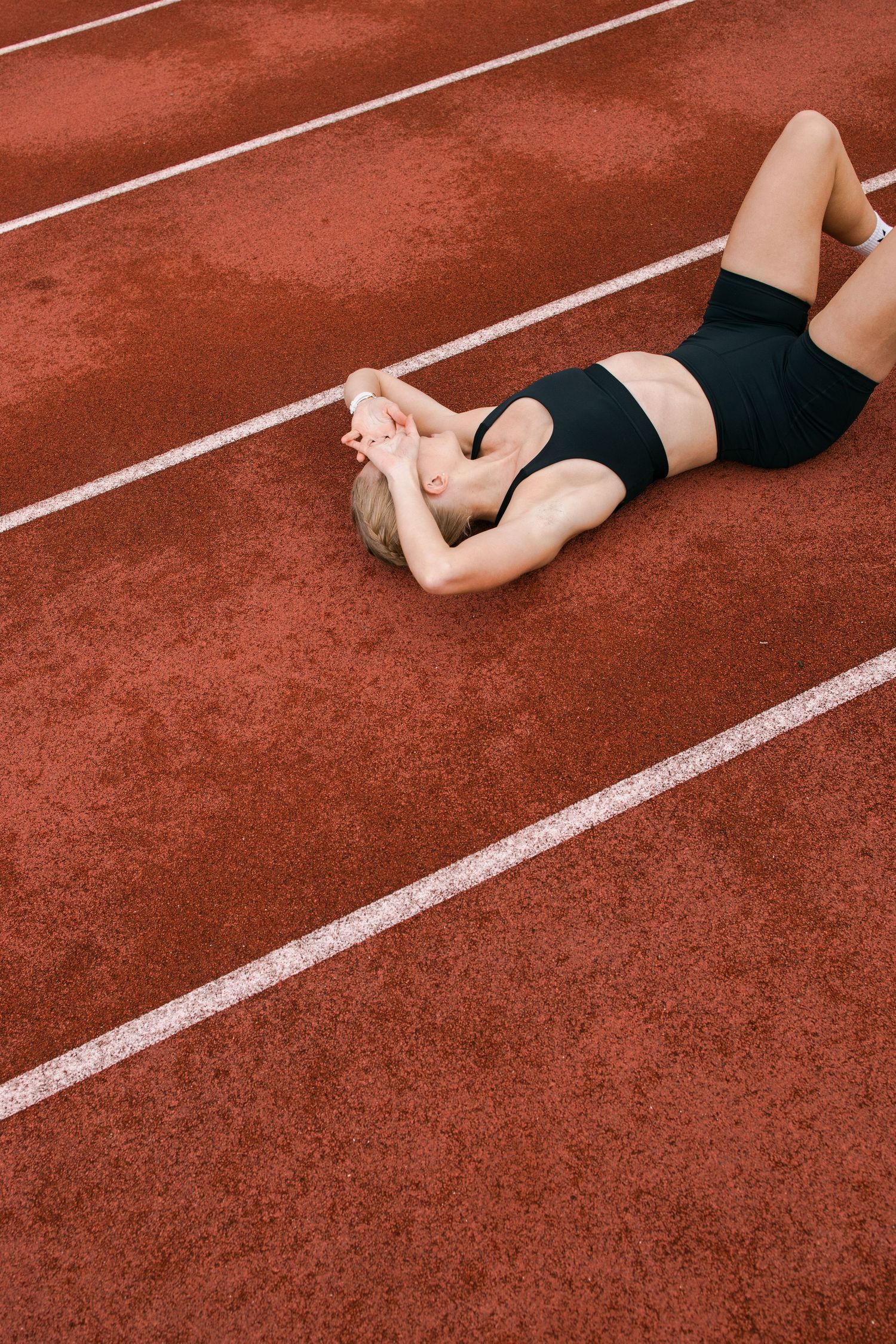 Close-up view of a person stretching on red running track with white lane markers at a sports facility.
