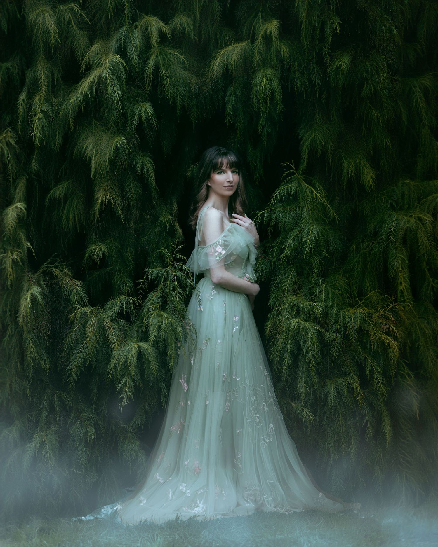 Dreamy scene of figure in flowing white gown standing among foggy evergreen trees.