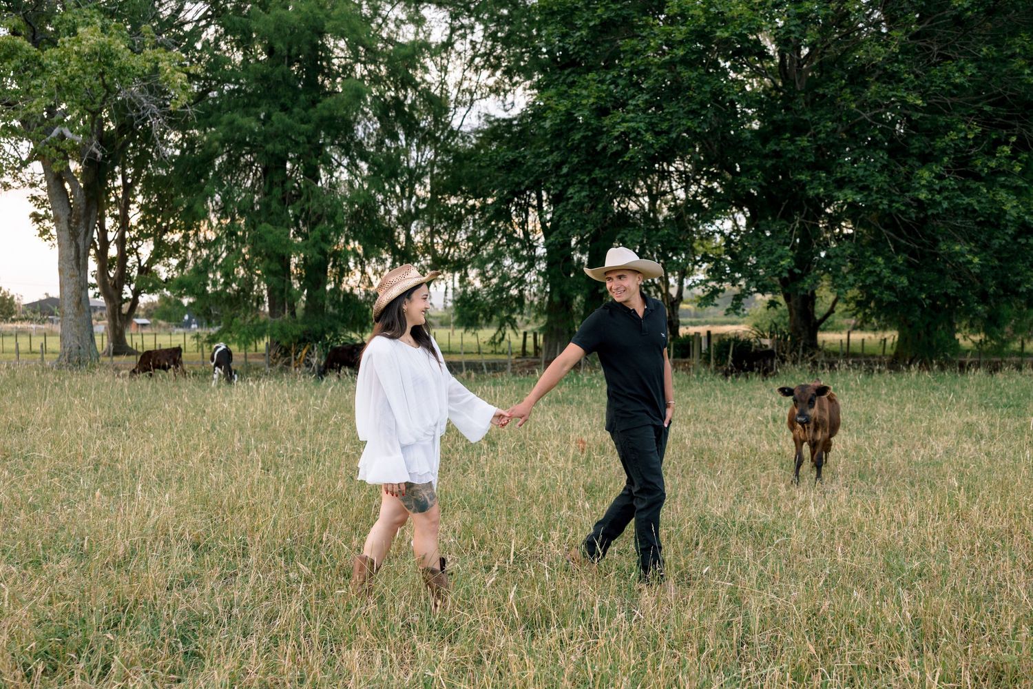 A couple walks hand in hand through a grassy field with their dog following behind.