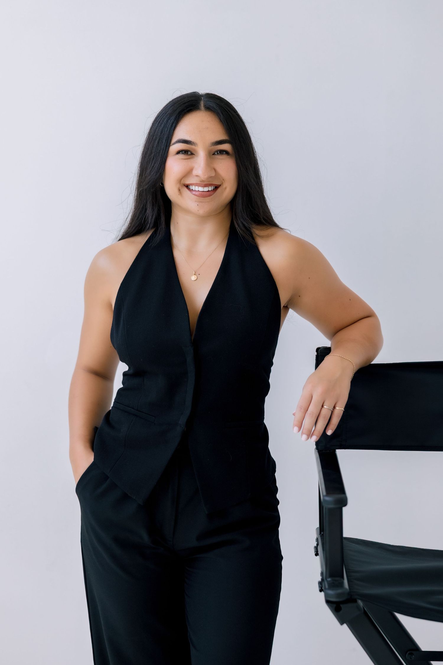 Professional portrait against white background showing someone in an elegant black halter top and pants with a warm smile.