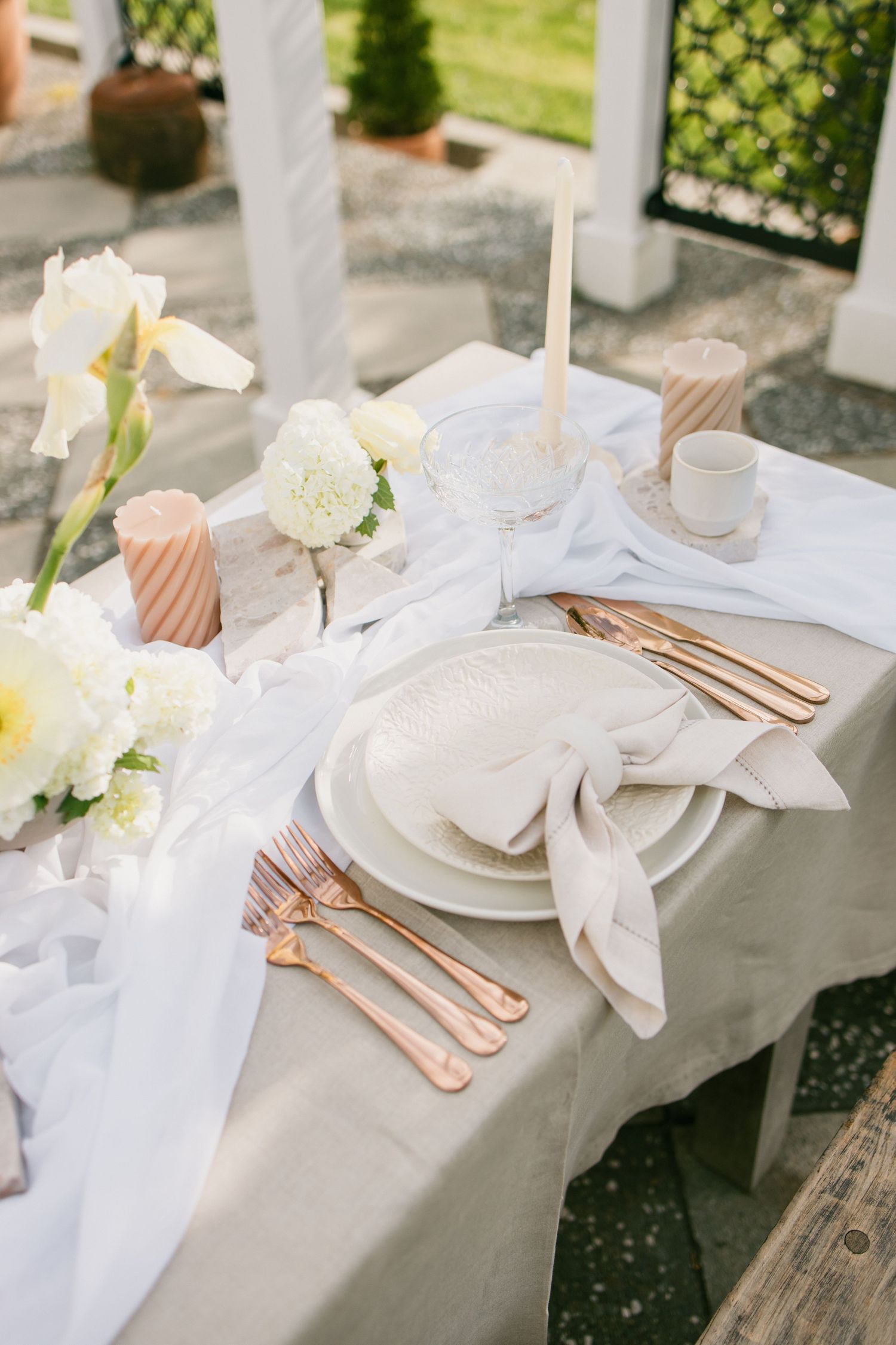 Elegant white and rose gold table setting with soft ethereal fabric draping and white floral accents for a luxurious event.