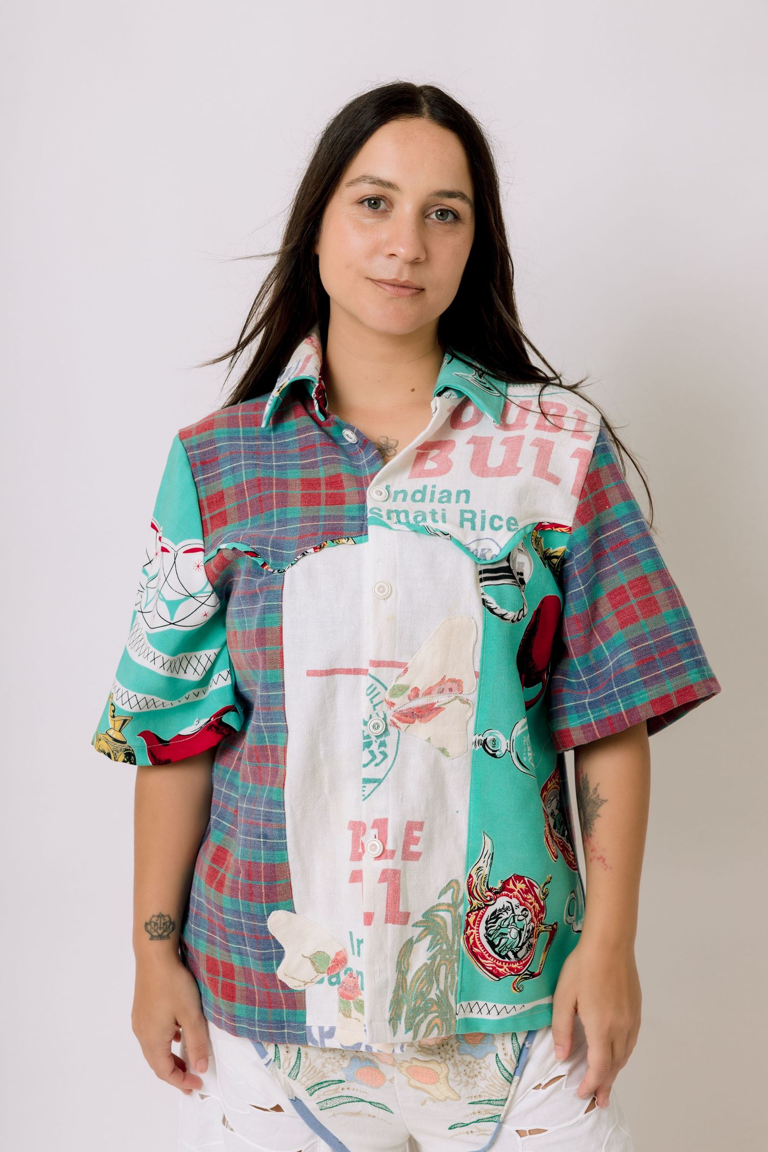 Person wearing a plaid short-sleeve button-up shirt holding up upcycled tote bags with retro designs.