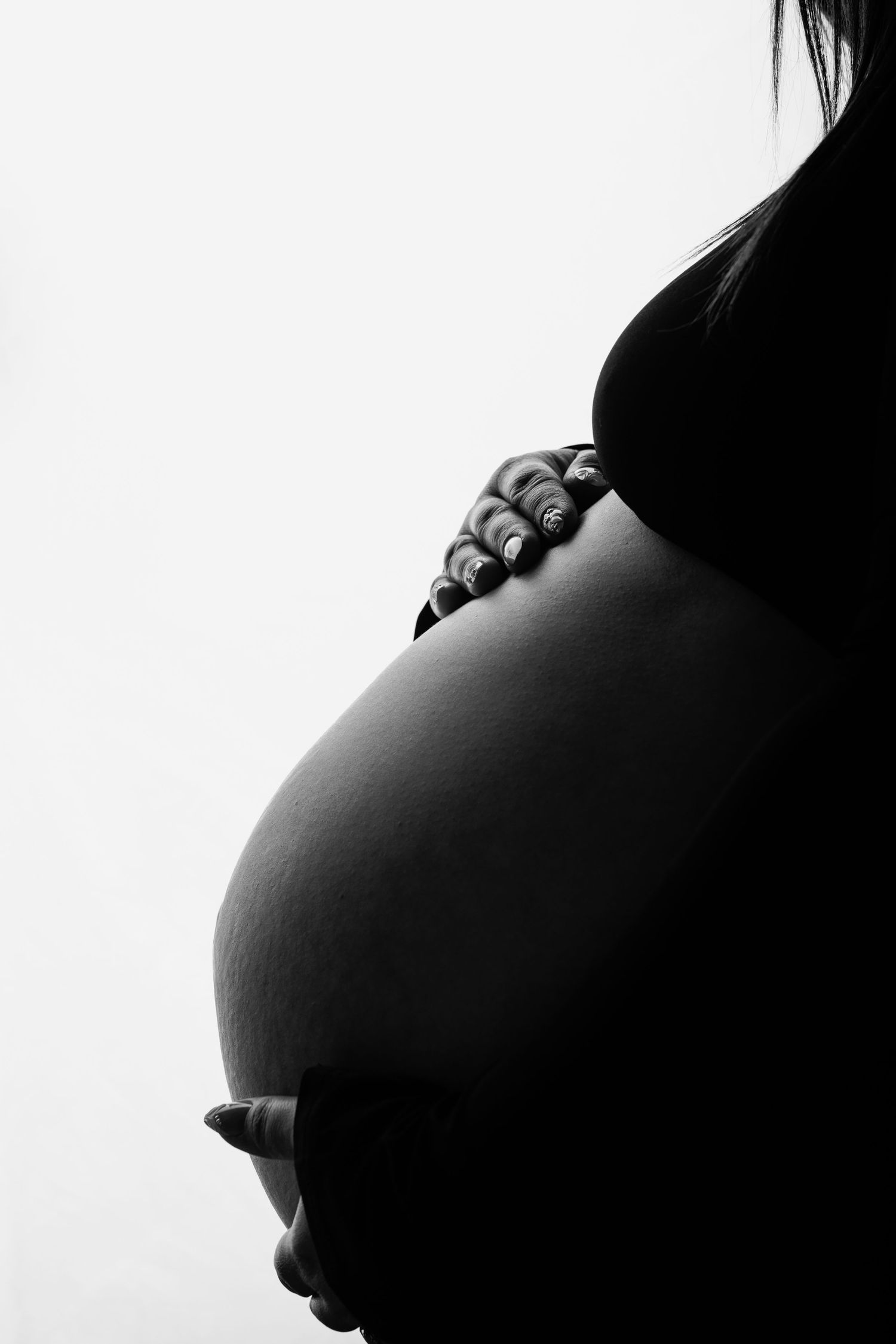 Black and white silhouette of a pregnant woman cradling her bare baby bump with both hands.
