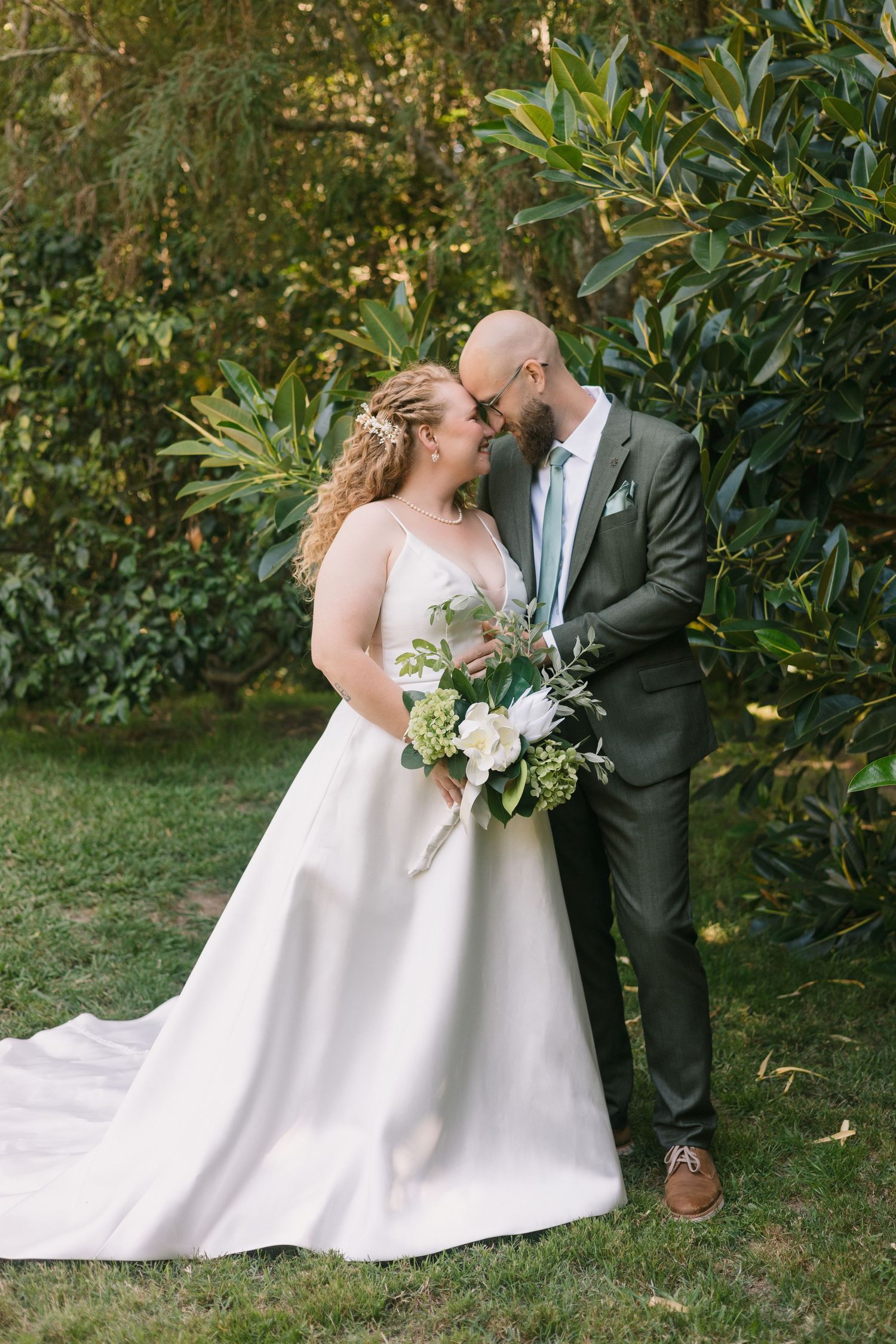 Romantic wedding portrait of couple embracing outdoors in garden setting with lush greenery.