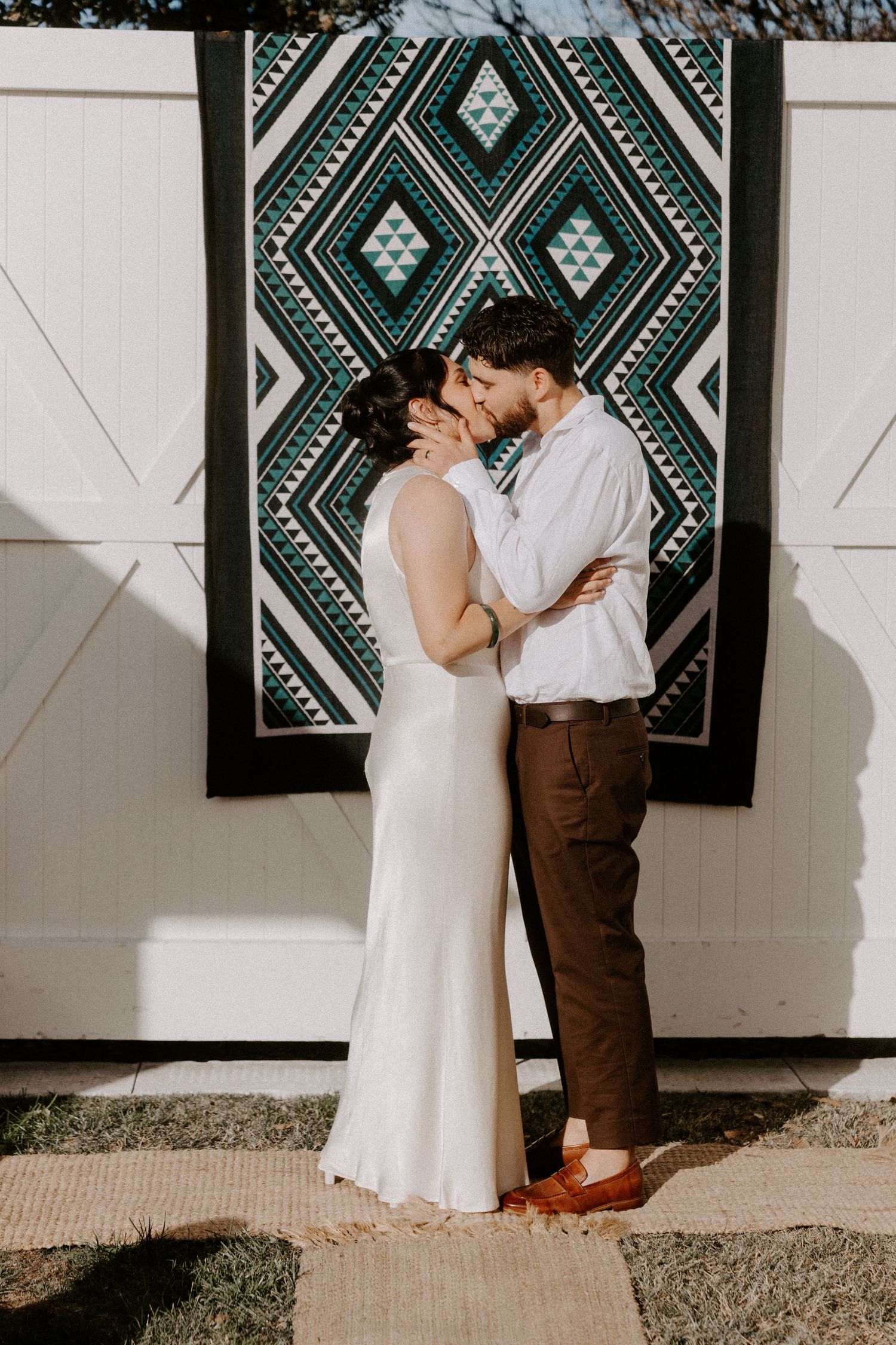 Couple embraces against a geometric patterned tapestry with blue and white diamond designs.