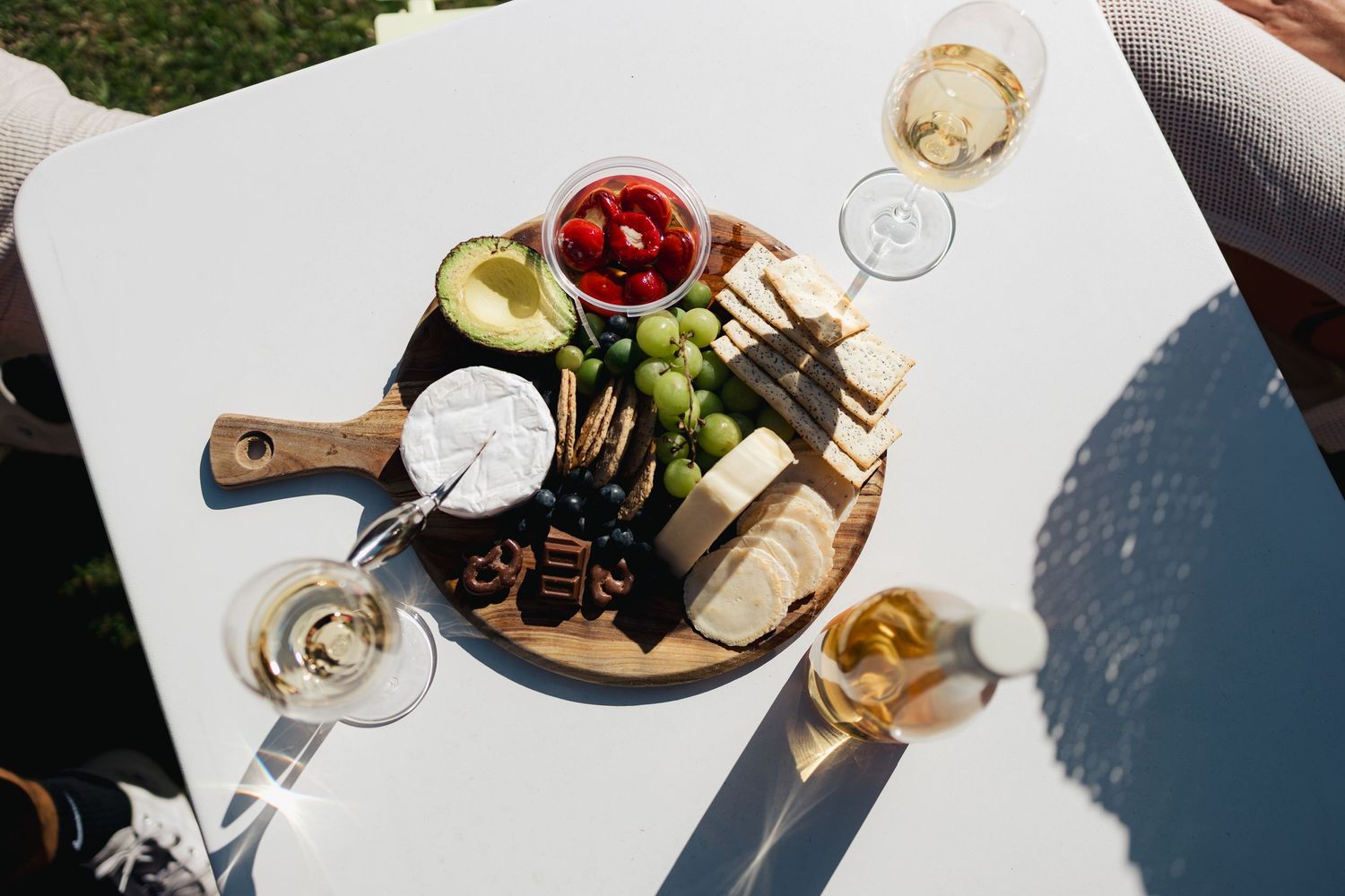Overhead view of charcuterie board with wine glasses and snacks on white table.