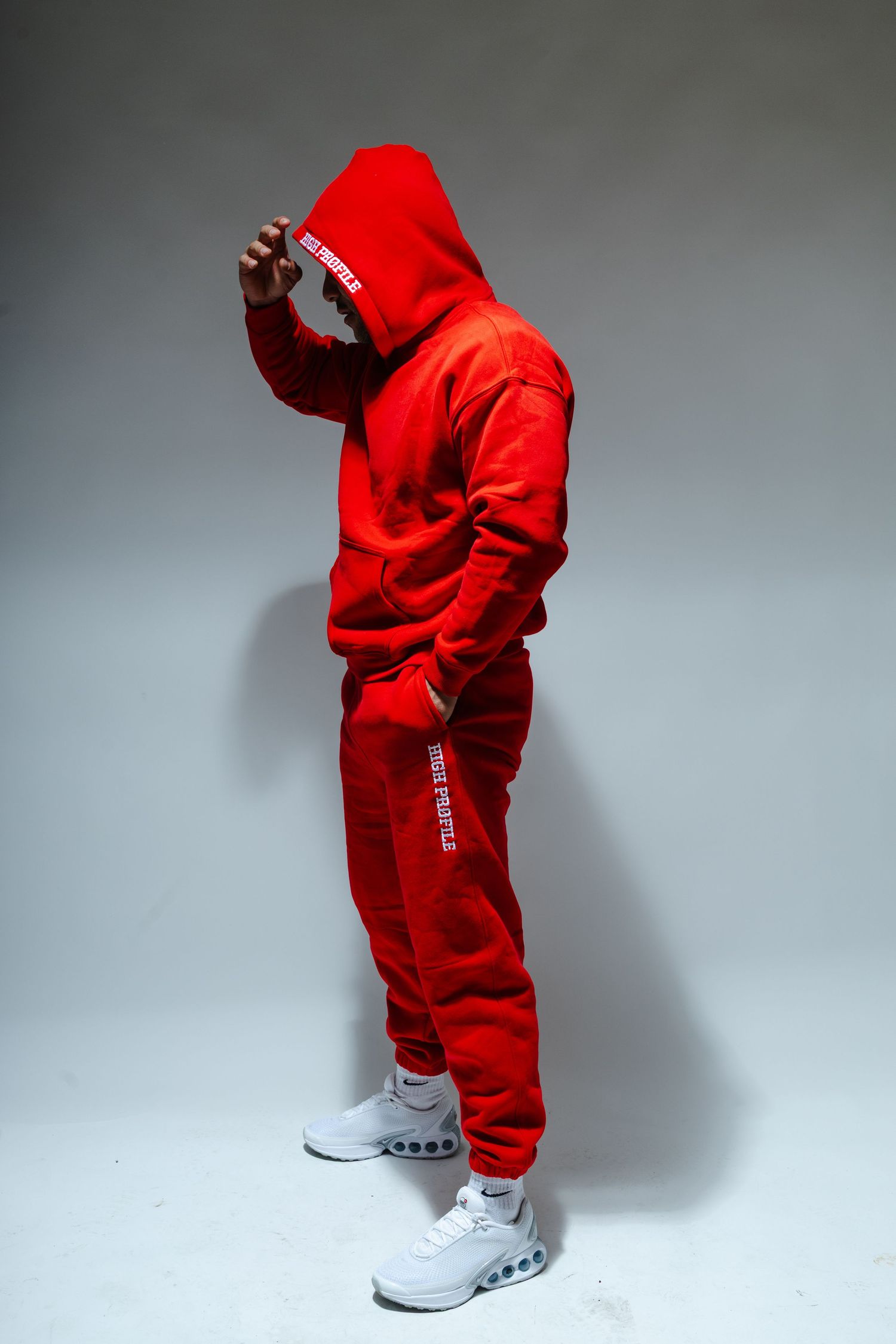 Person wearing bright red tracksuit and white sneakers poses against gray studio backdrop.