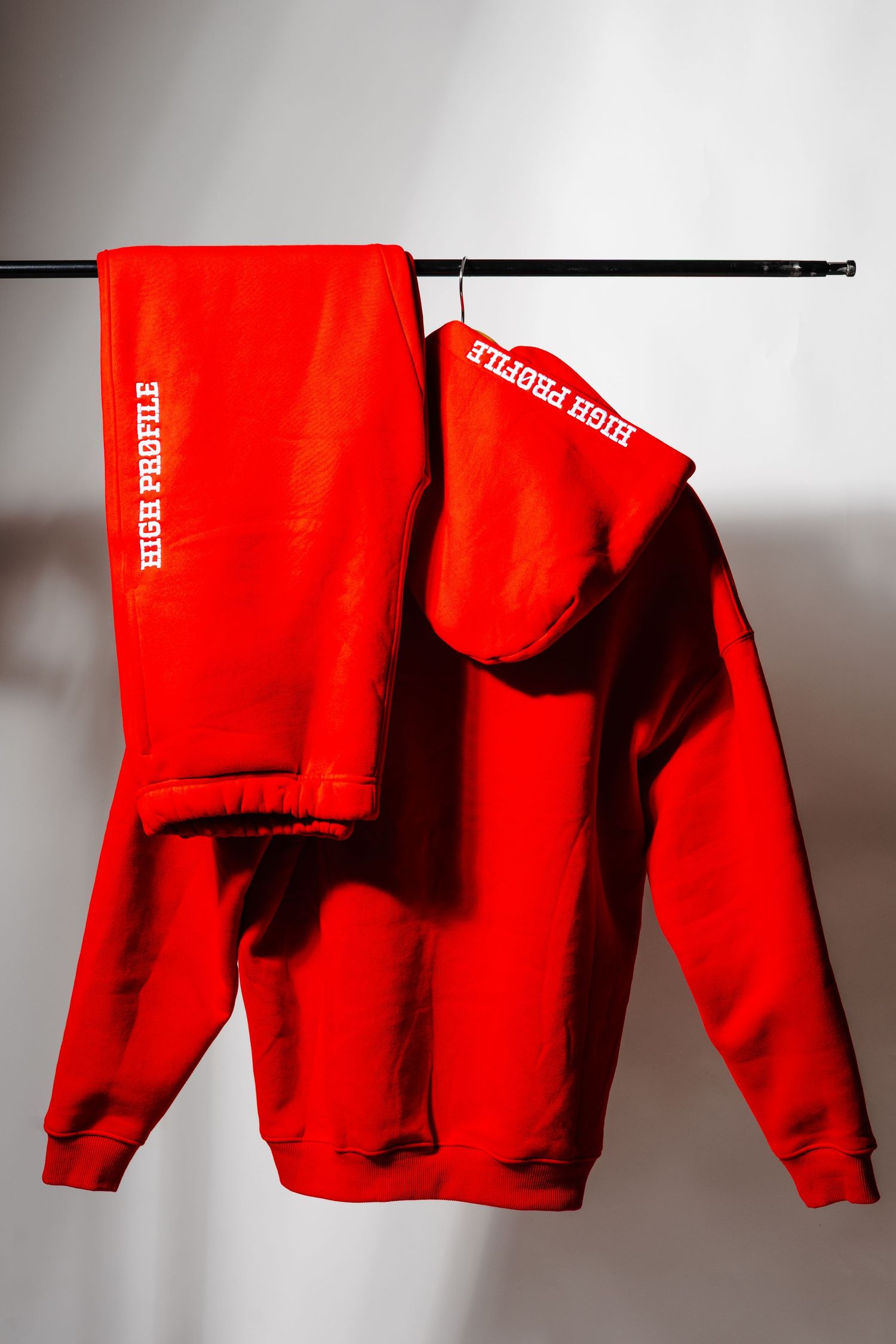 Red sweatsuit pieces hanging on black clothing rack showing athletic streetwear design.