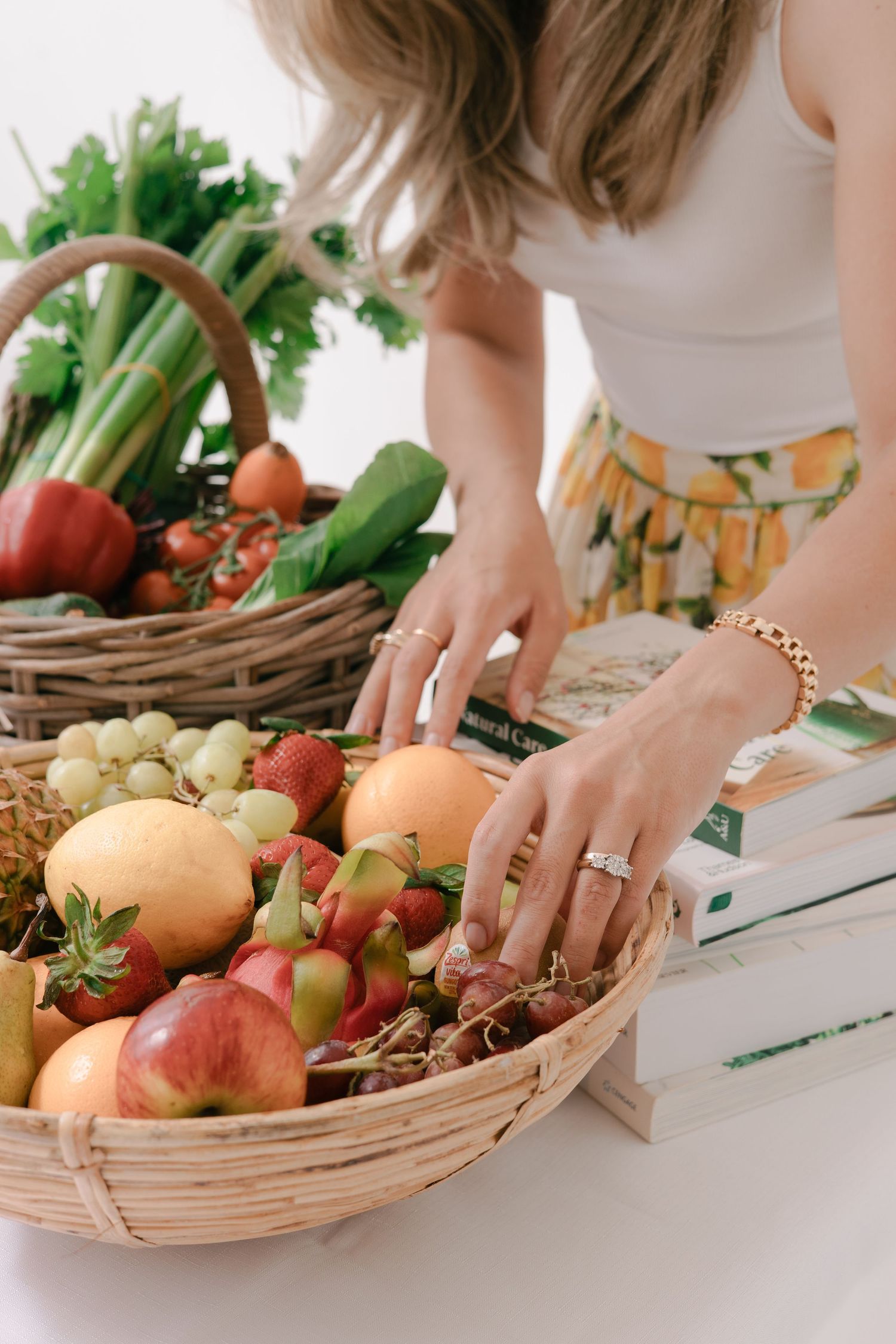 Hands chopping fresh vegetables and fruits on a white cutting board next to a woven basket filled with produce.