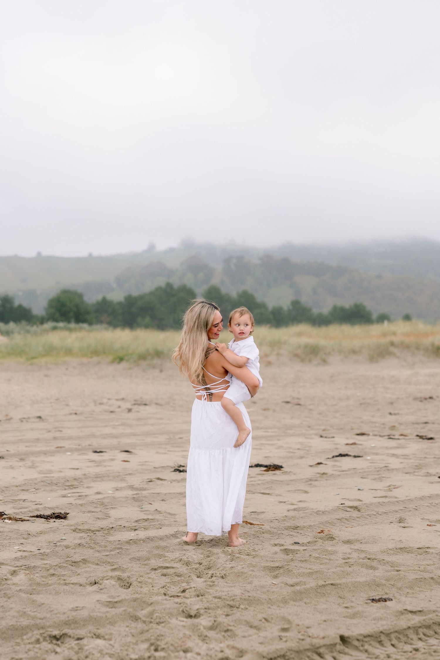 A family in white dresses walks along a misty beach on an overcast day.