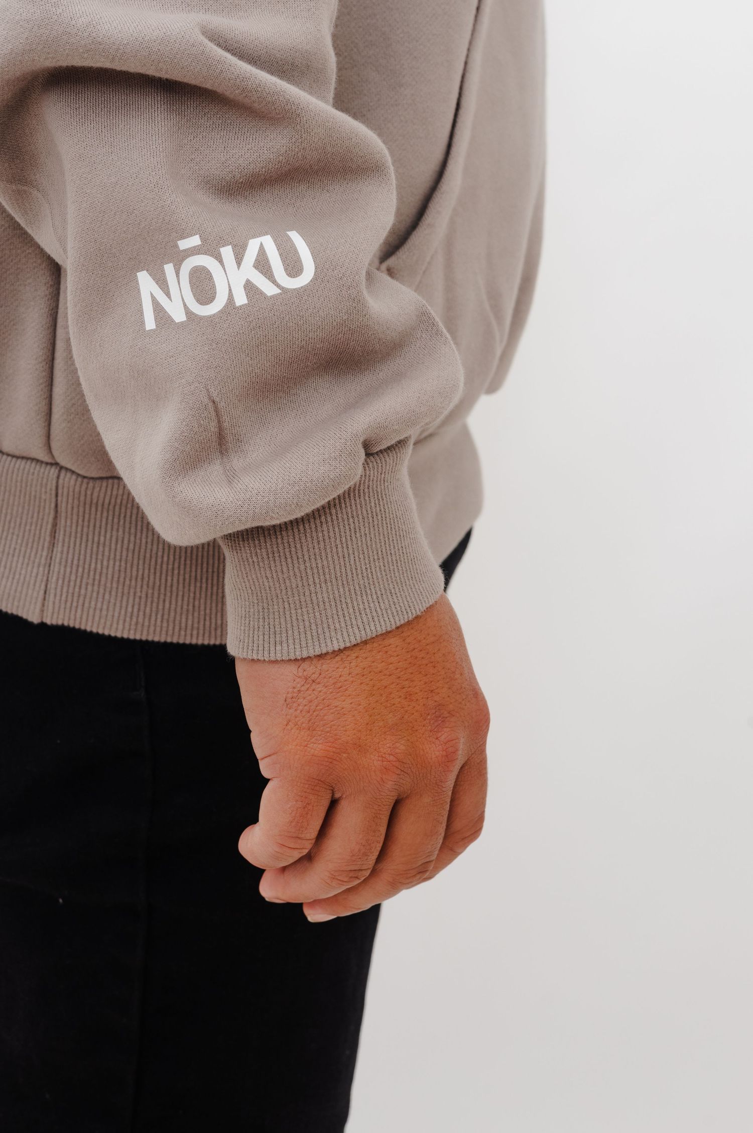 Close-up of a beige sweatshirt sleeve with white NOKU text branding against a light background.