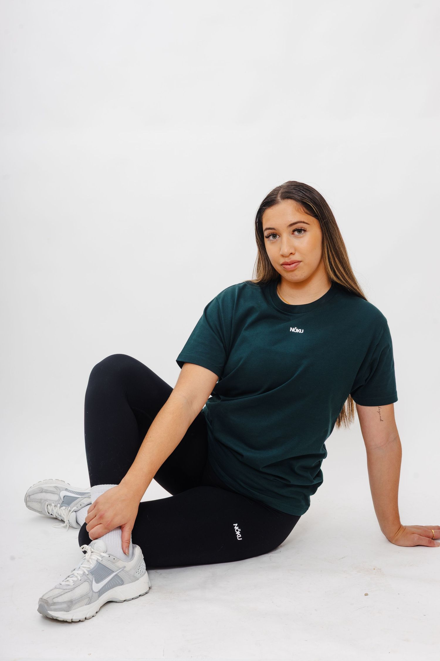Person in black t-shirt and pants lounging on white floor wearing silver sneakers in casual poses.